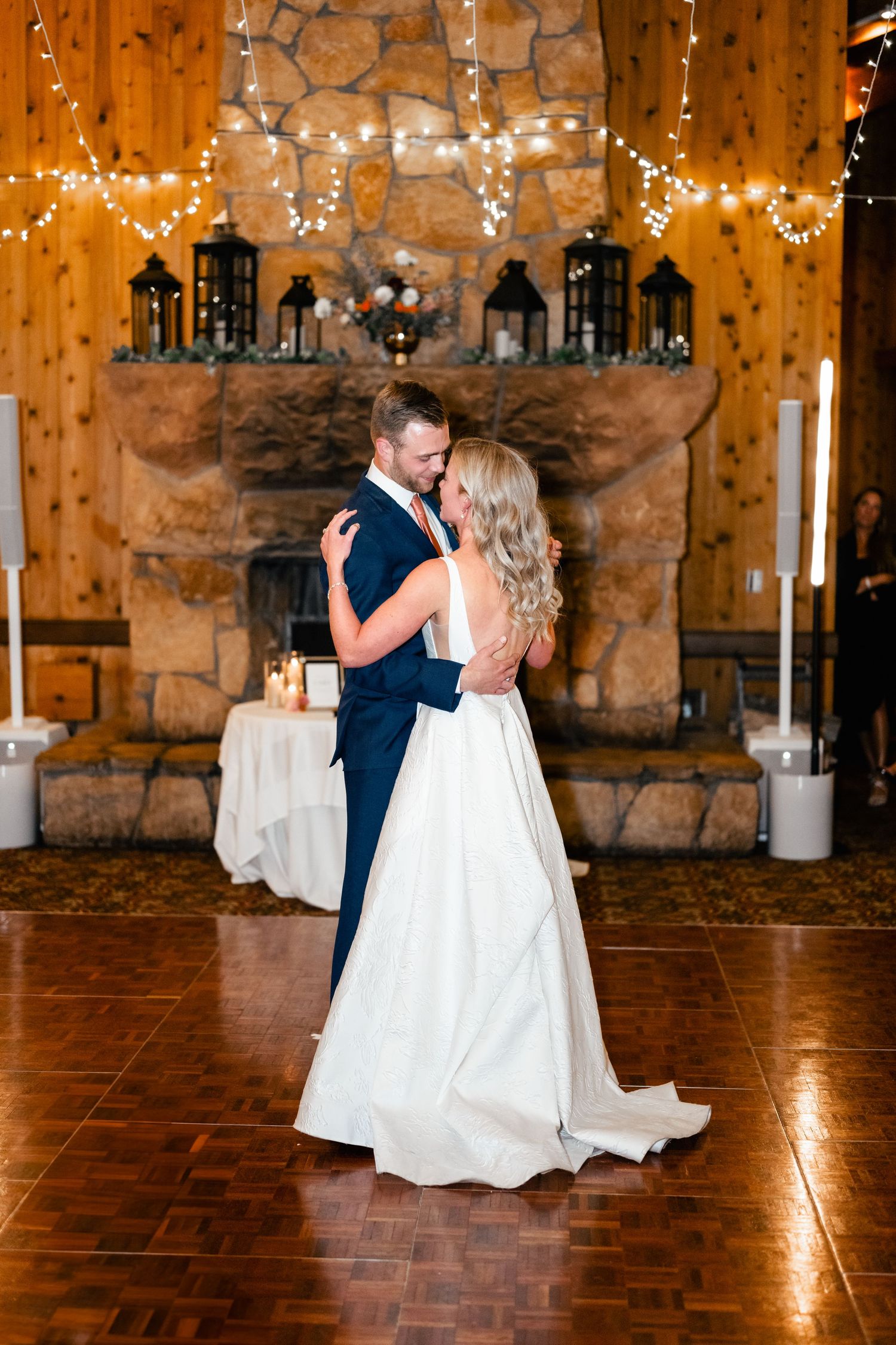 Couple dancing in front of a stone fireplace decorated with lanterns and fairy lights at their reception. Park City Wedding Photographer.