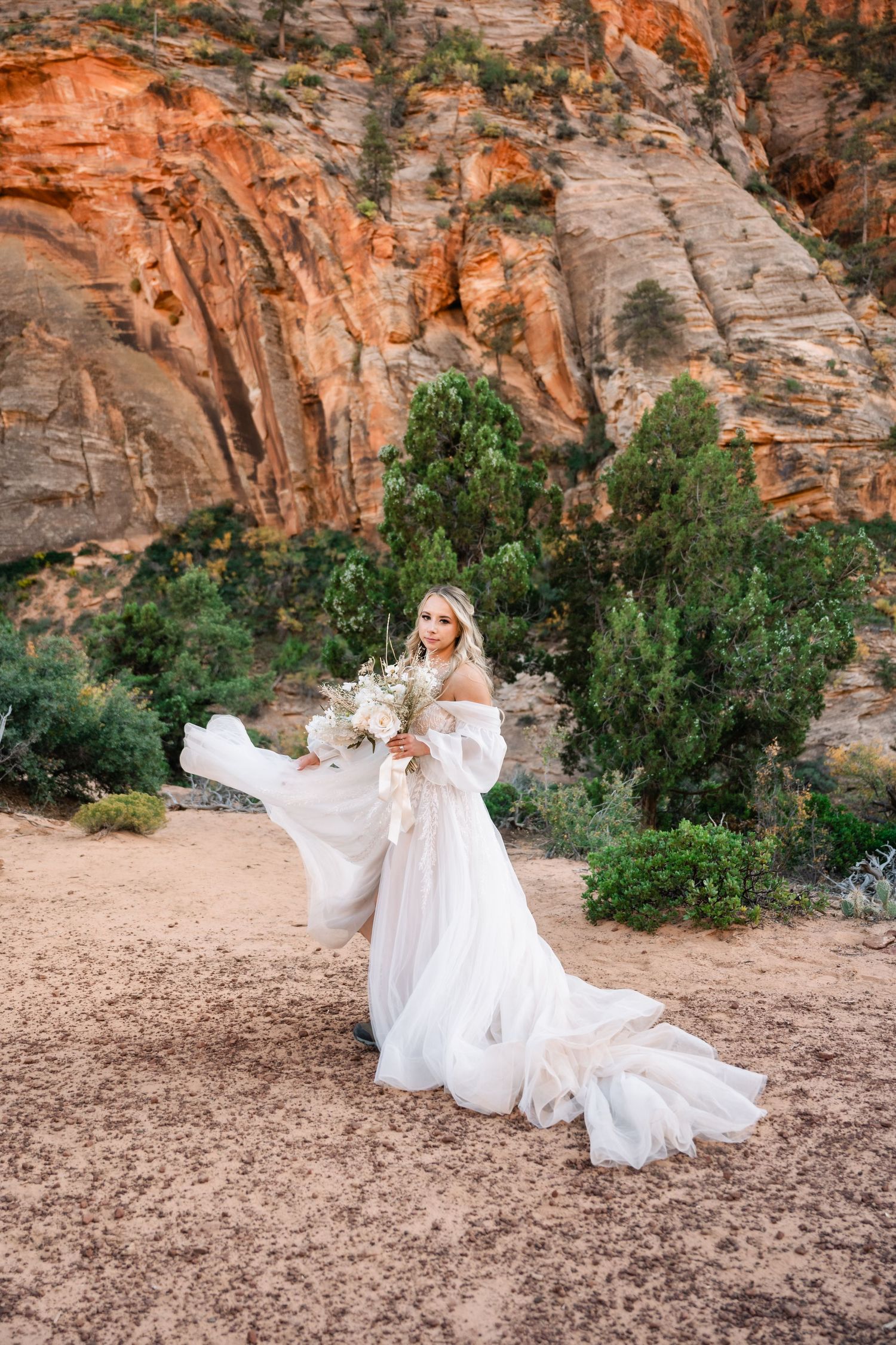 An ethereal bridal portrait with flowing white dress against dramatic red canyon walls.