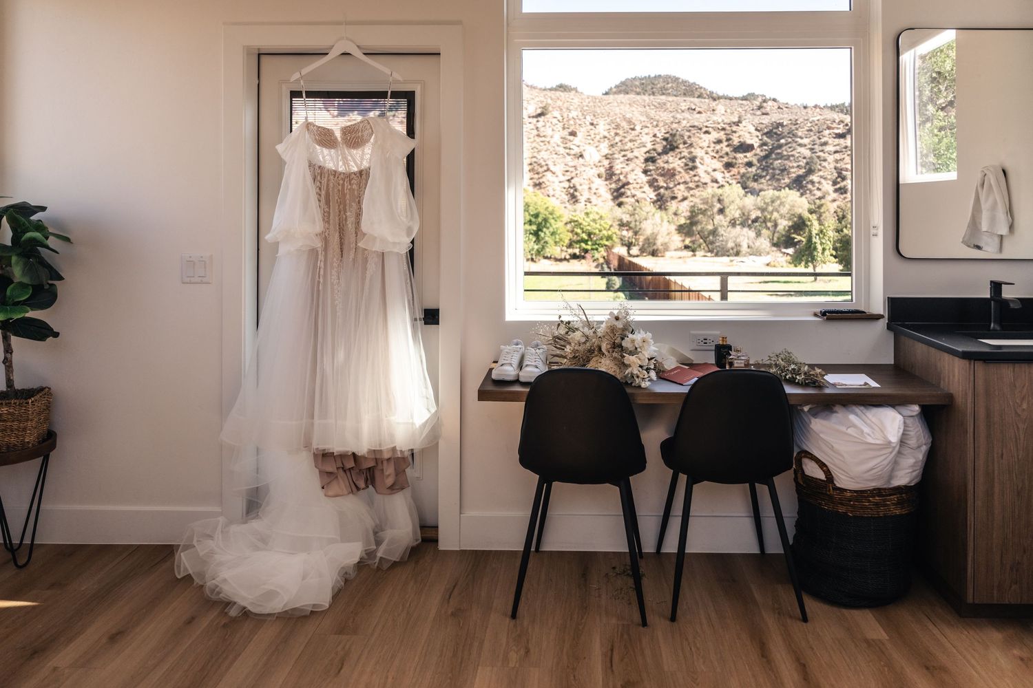 Elegant white wedding gown displayed against window with desert mountain landscape view.