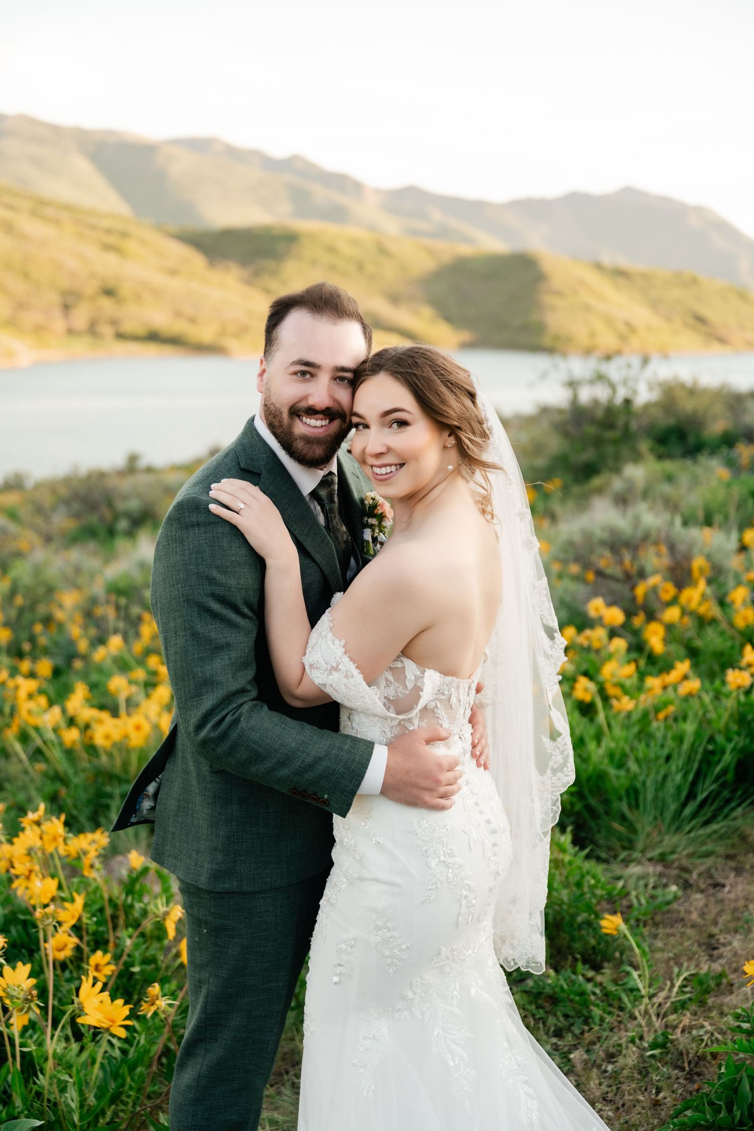 Newlyweds share an intimate moment among yellow wildflowers with a lake and mountains behind them.