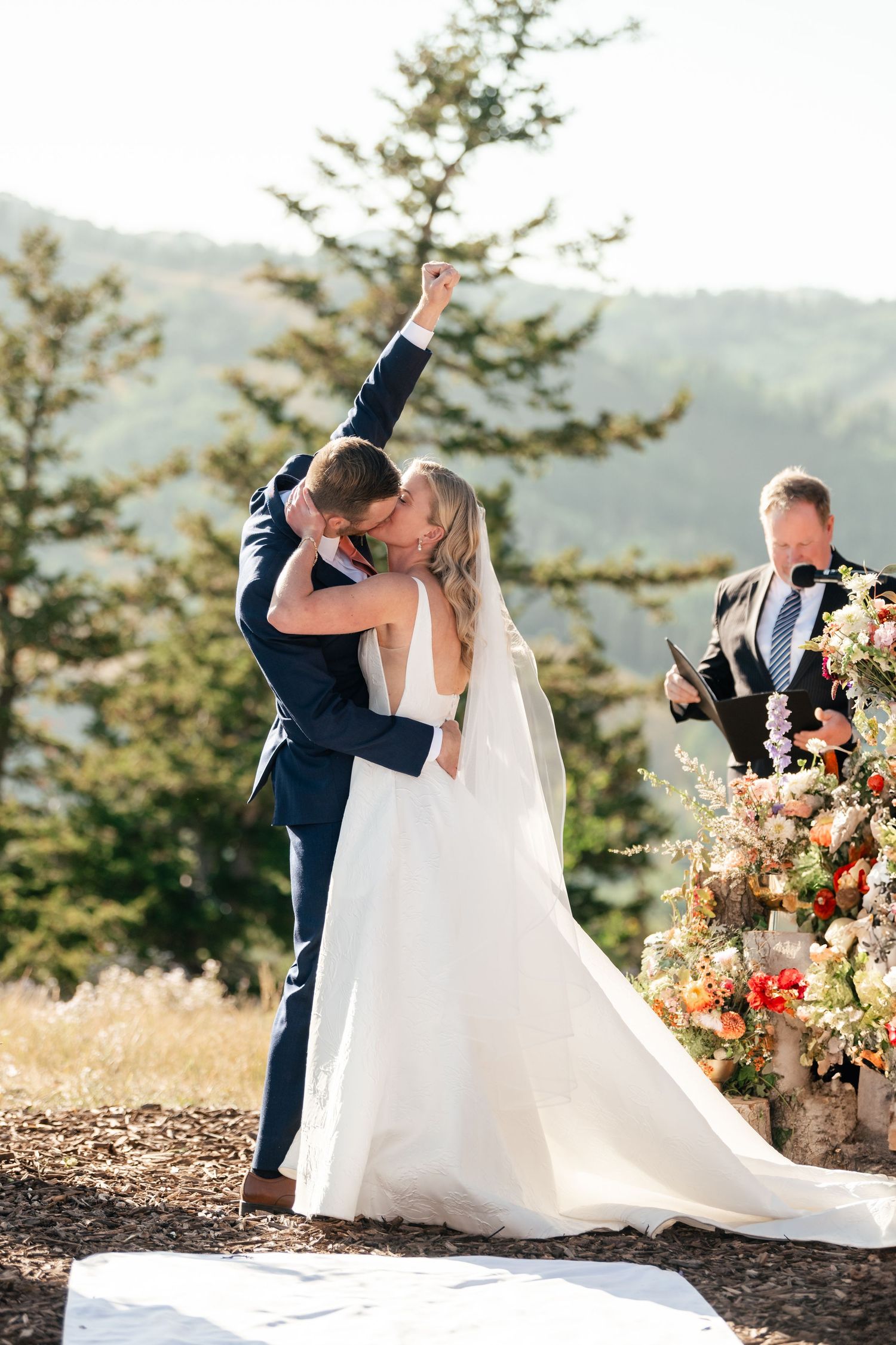 Newlyweds share romantic moment during mountain ceremony with officiant and floral arch at sunset. Park City Wedding Photographer.