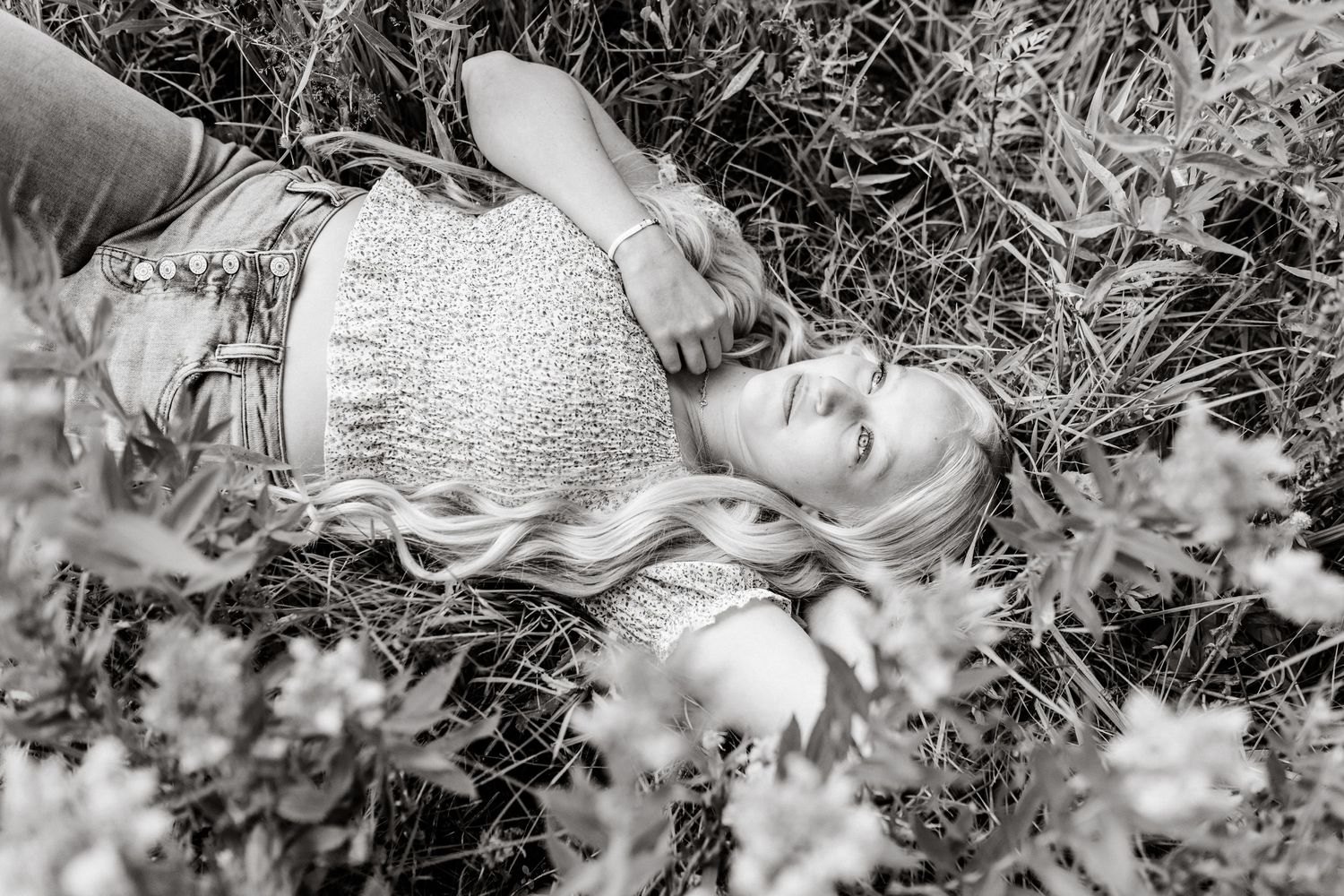 black and white senior portrait of a senior girl lying in a wildflower meadow