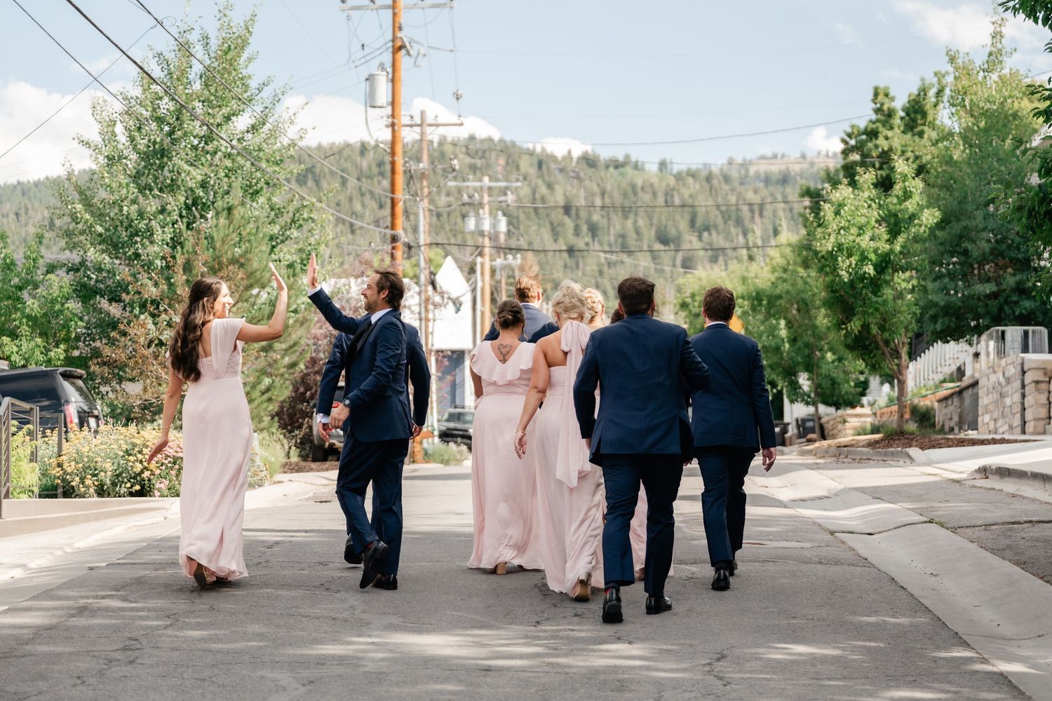 Wedding party walking together on sloped residential street with mountain landscape behind.