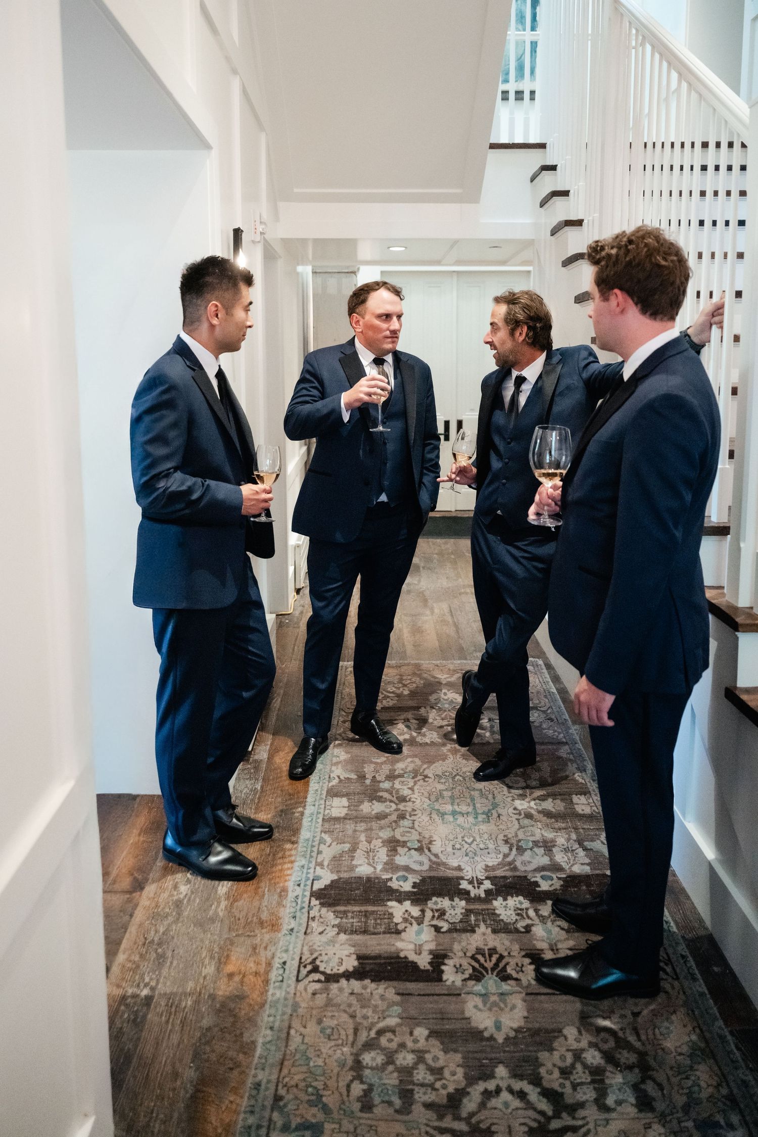 Groomsmen in navy suits gather for conversation on a rustic hardwood floor.