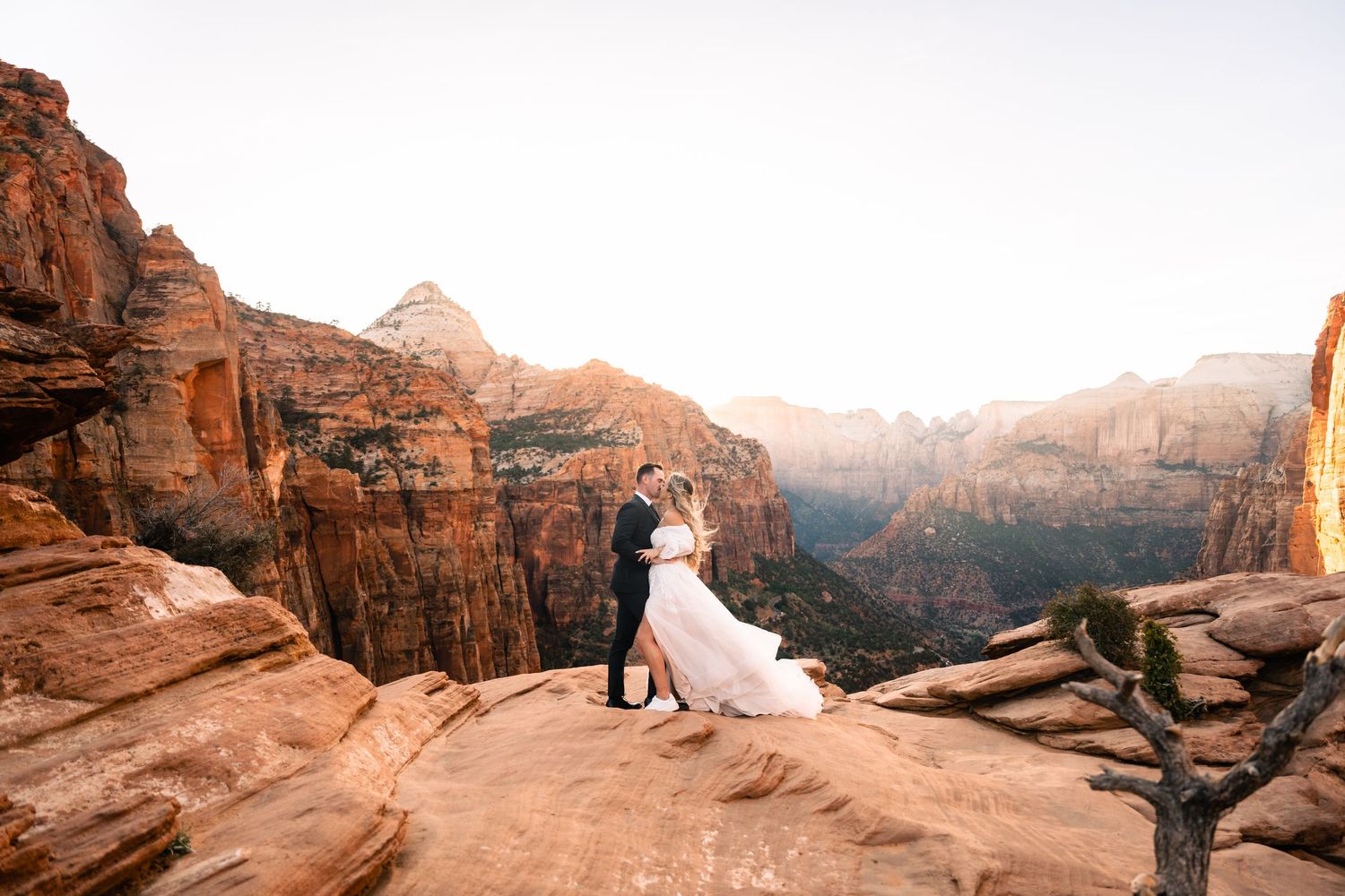 Bride and Groom in wedding attire kiss at the Zion Overlook at sunset. Zion Utah Wedding Photographer. Utah Elopement Photographer.