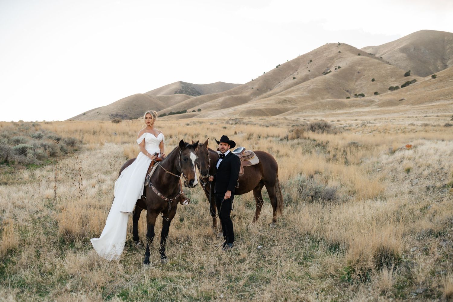 Two horses and wedding couple stand together in a scenic mountain landscape with golden grass and rolling hills. Utah wedding photographer.