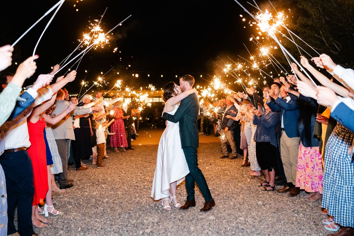 Wedding guests holding sparklers creating a magical light tunnel during nighttime celebration.