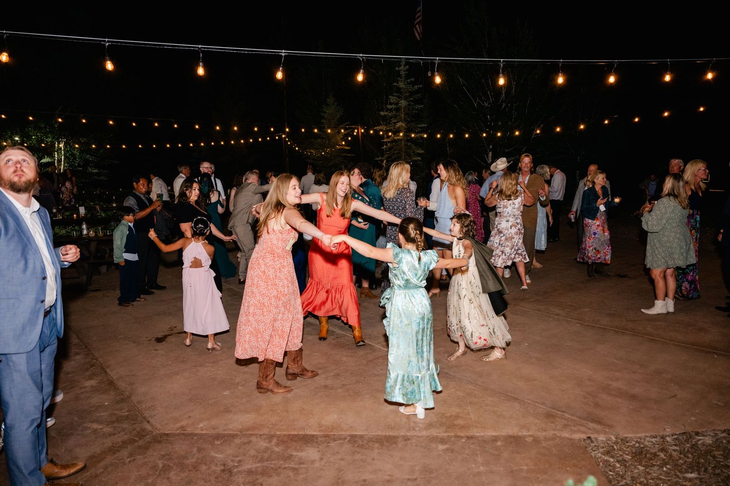 Wedding guests dancing under string lights at an outdoor evening reception.