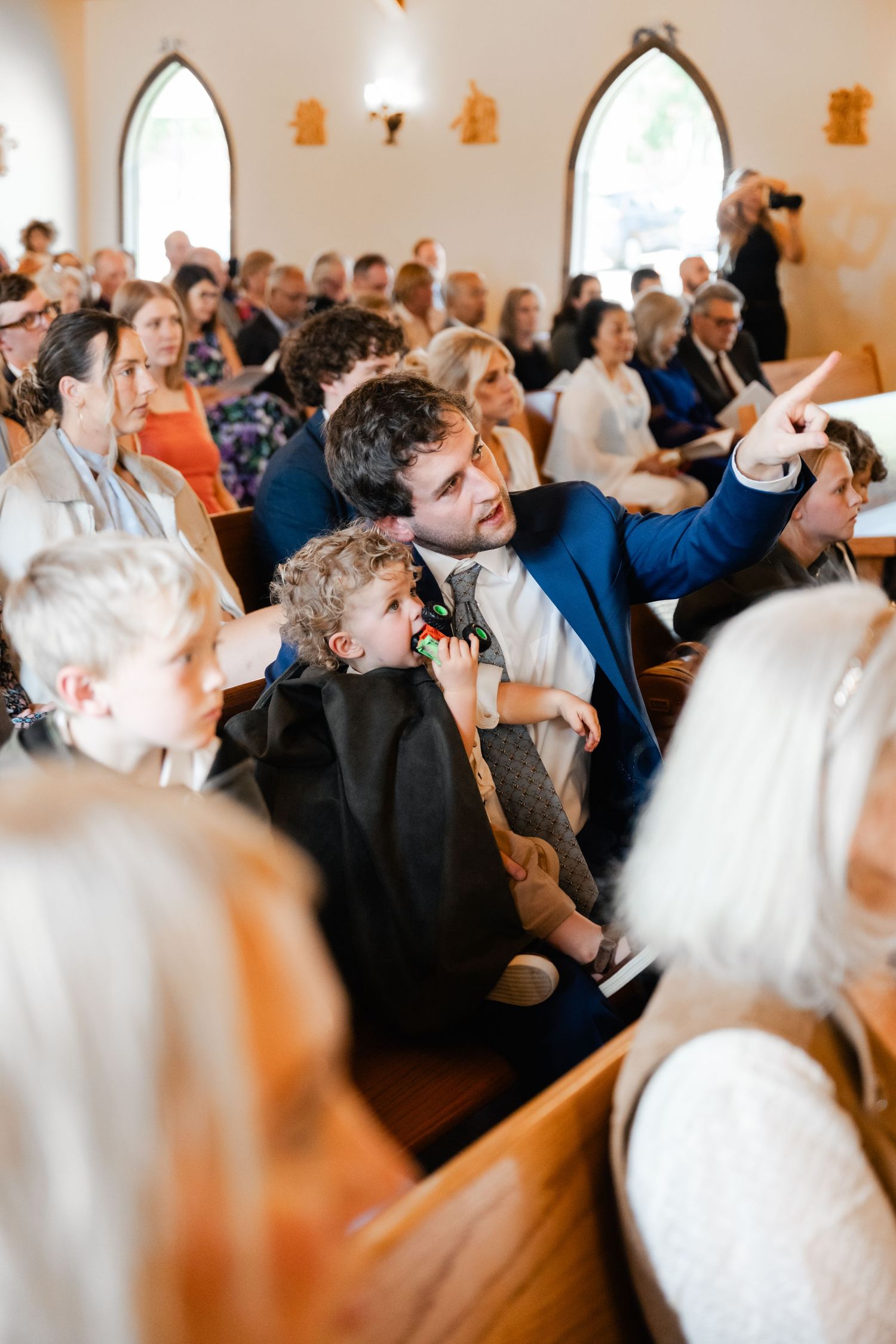 Wedding guests seated in wooden church pews react during ceremony.