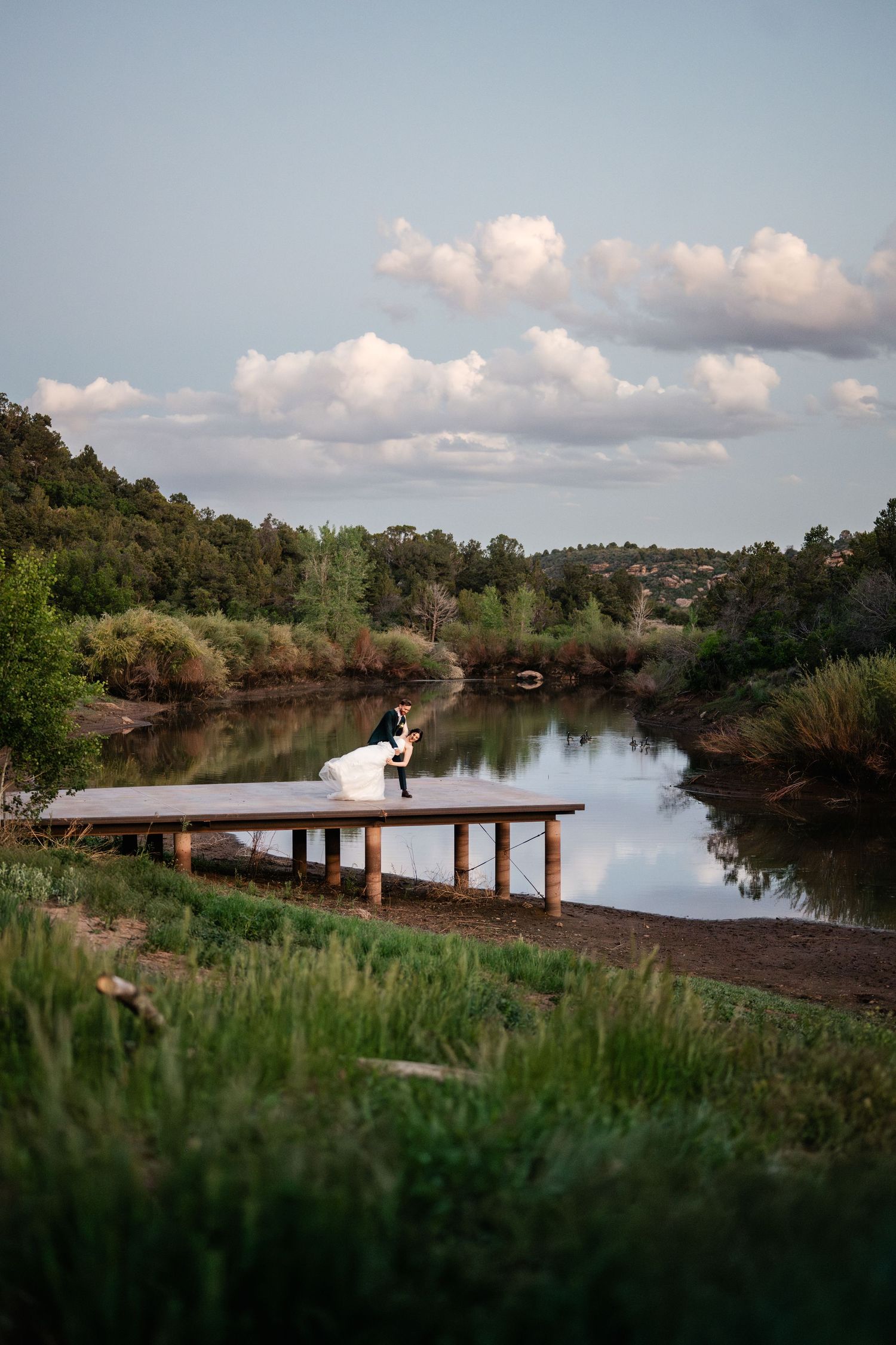Scenic lakeside wedding venue with wooden dock and lush greenery during golden hour.