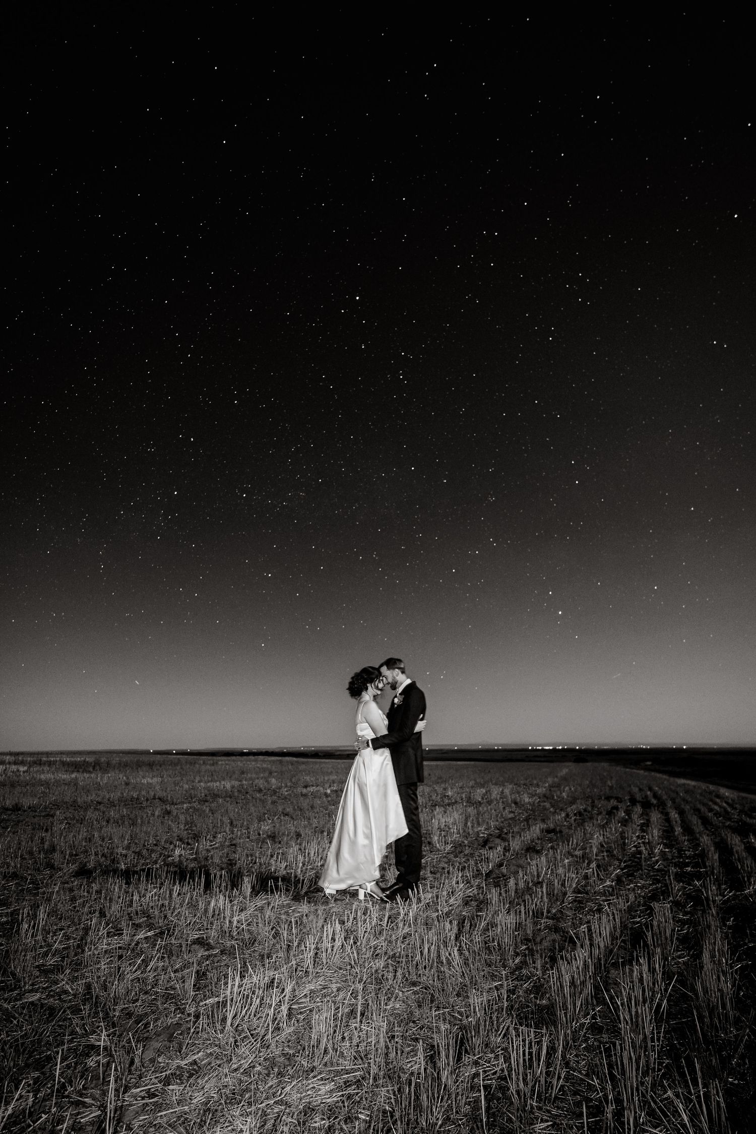 Dramatic black and white nighttime wedding portrait under starlit sky.