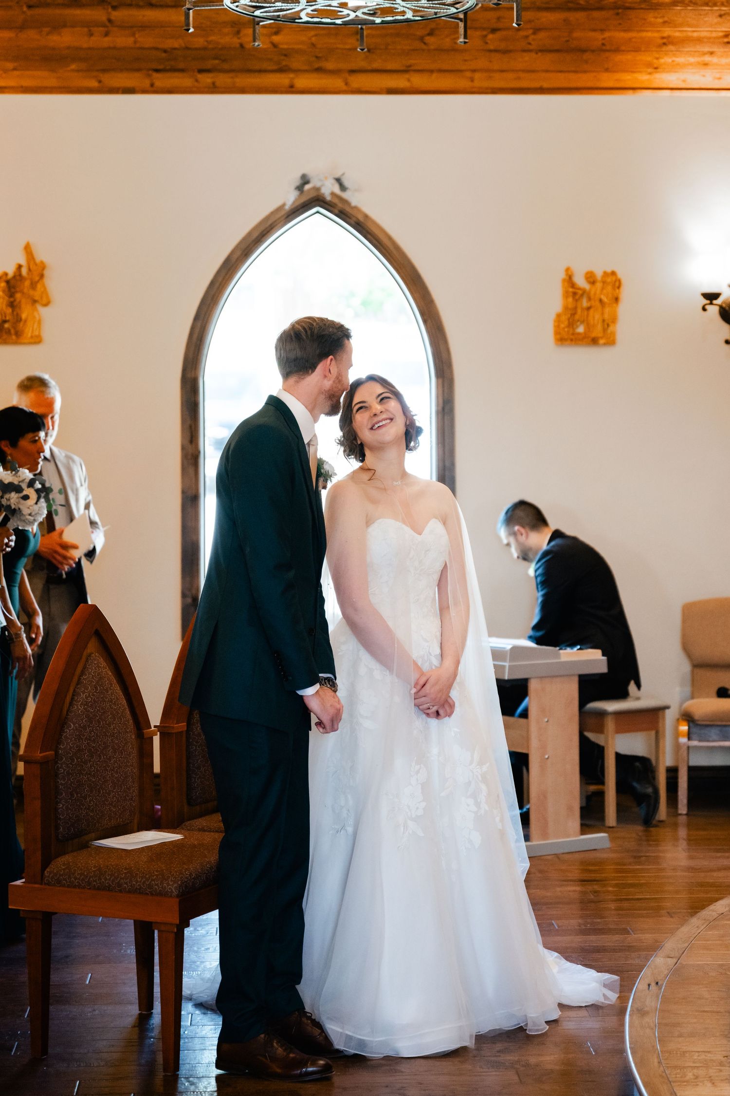 A wedding ceremony unfolds in a rustic church with wooden beams and arched windows.