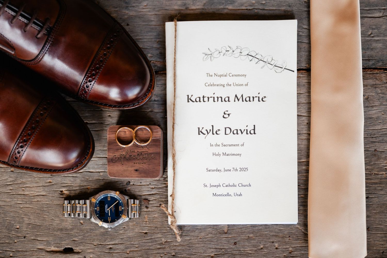 Wedding invitation and brown leather dress shoes arranged on rustic wooden surface.
