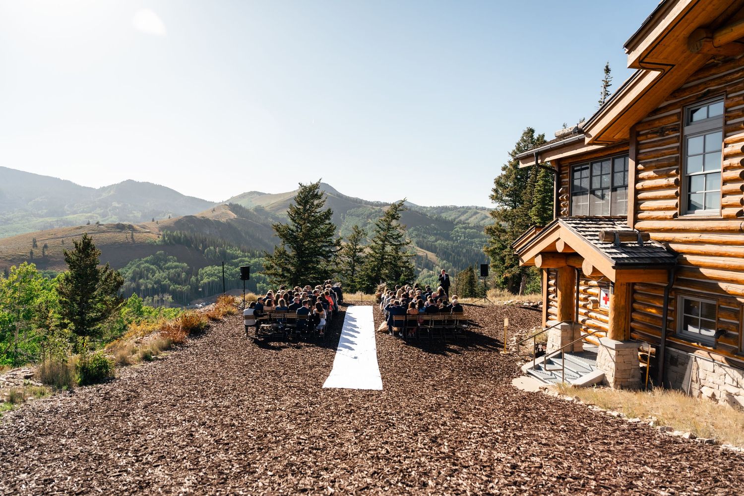 Outdoor wedding ceremony setup with mountain views at rustic log cabin venue with gravel ground and evergreen trees.