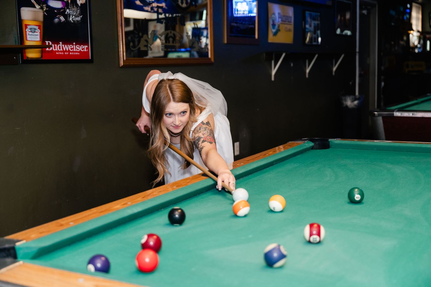 A player lines up a shot on a pool table with colorful billiard balls scattered across the green felt surface.