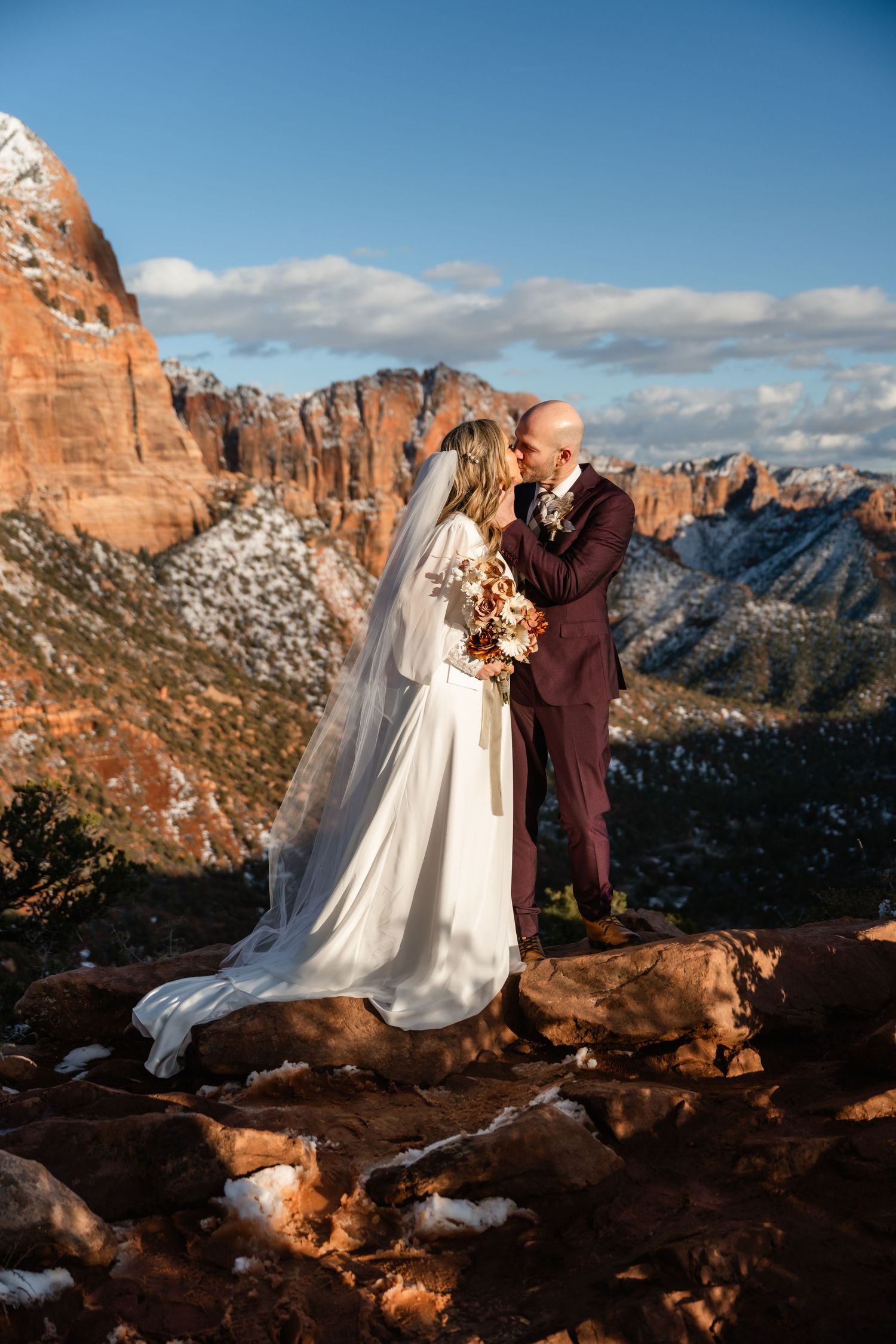 A couple shares an intimate moment during their wedding photoshoot against a stunning red rock mountain landscape at sunset.