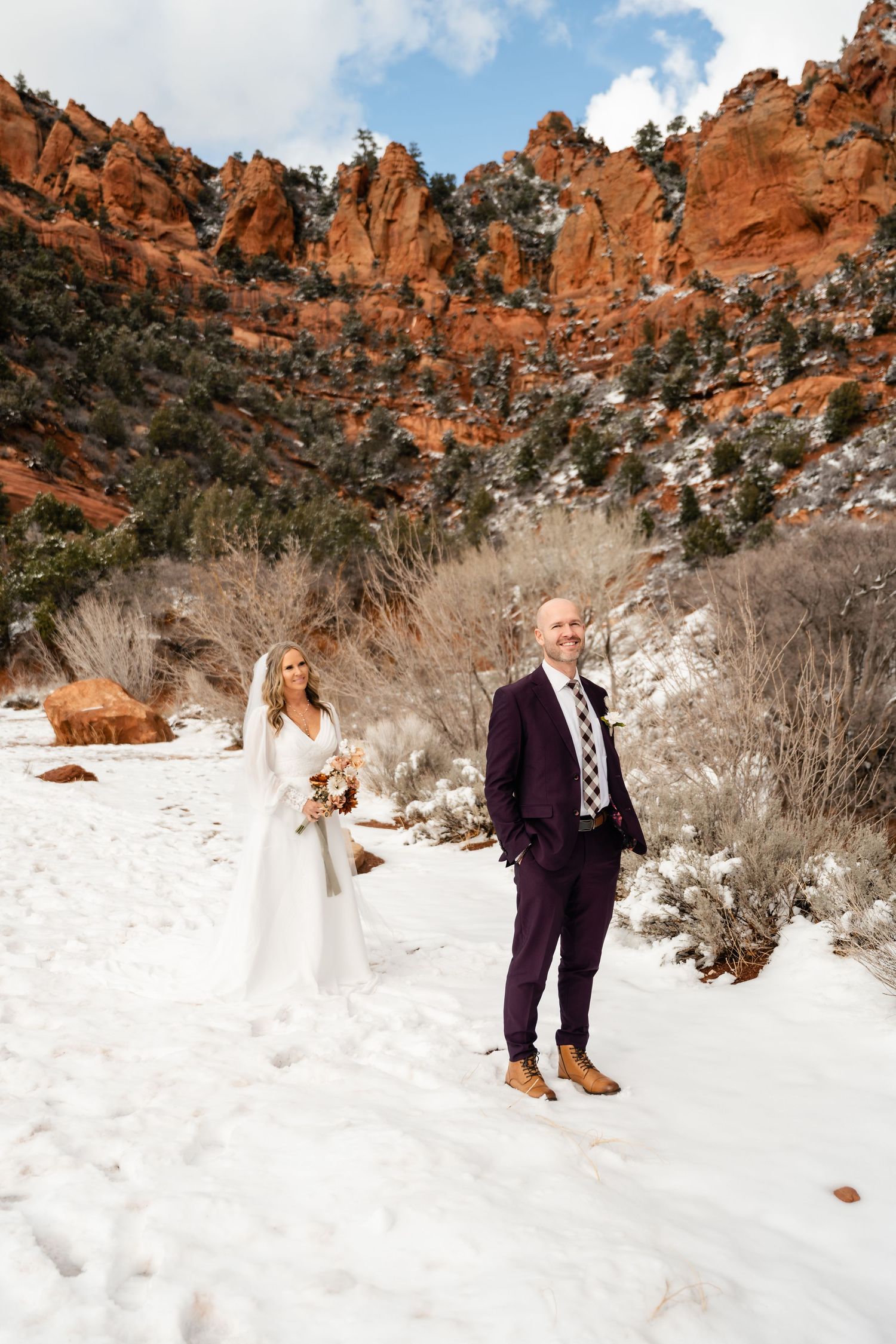 A winter wedding photo with snow-covered red rock formations in Zion National Park.