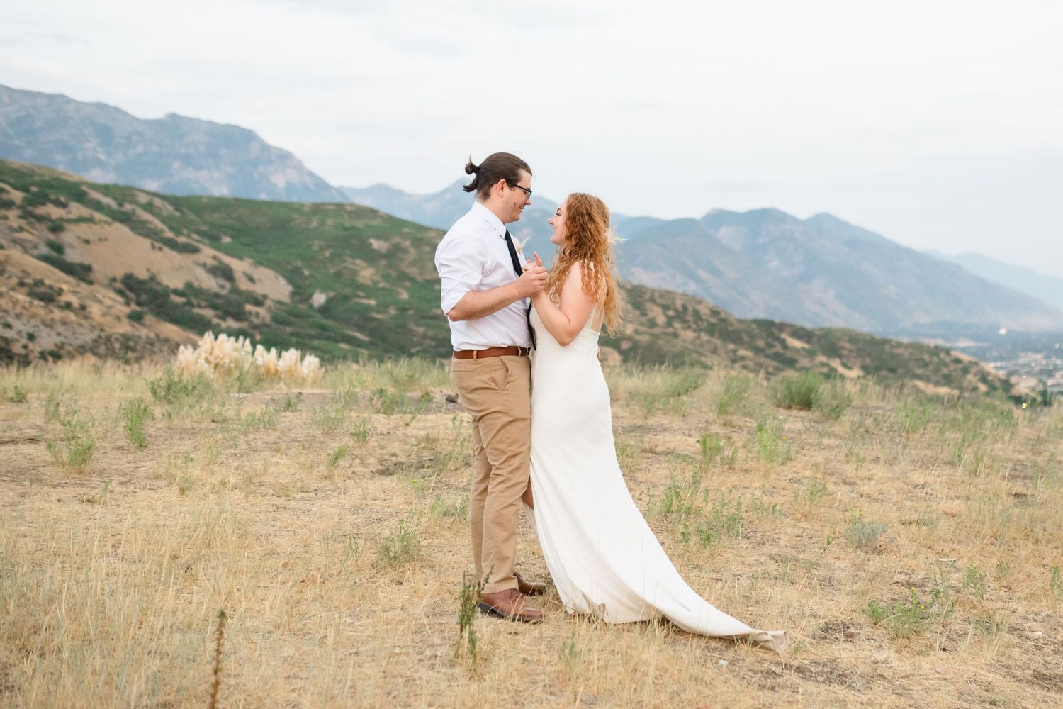 A couple embraces on a mountainside during their wedding photoshoot with scenic mountain ranges in the background. Utah mountain elopement.