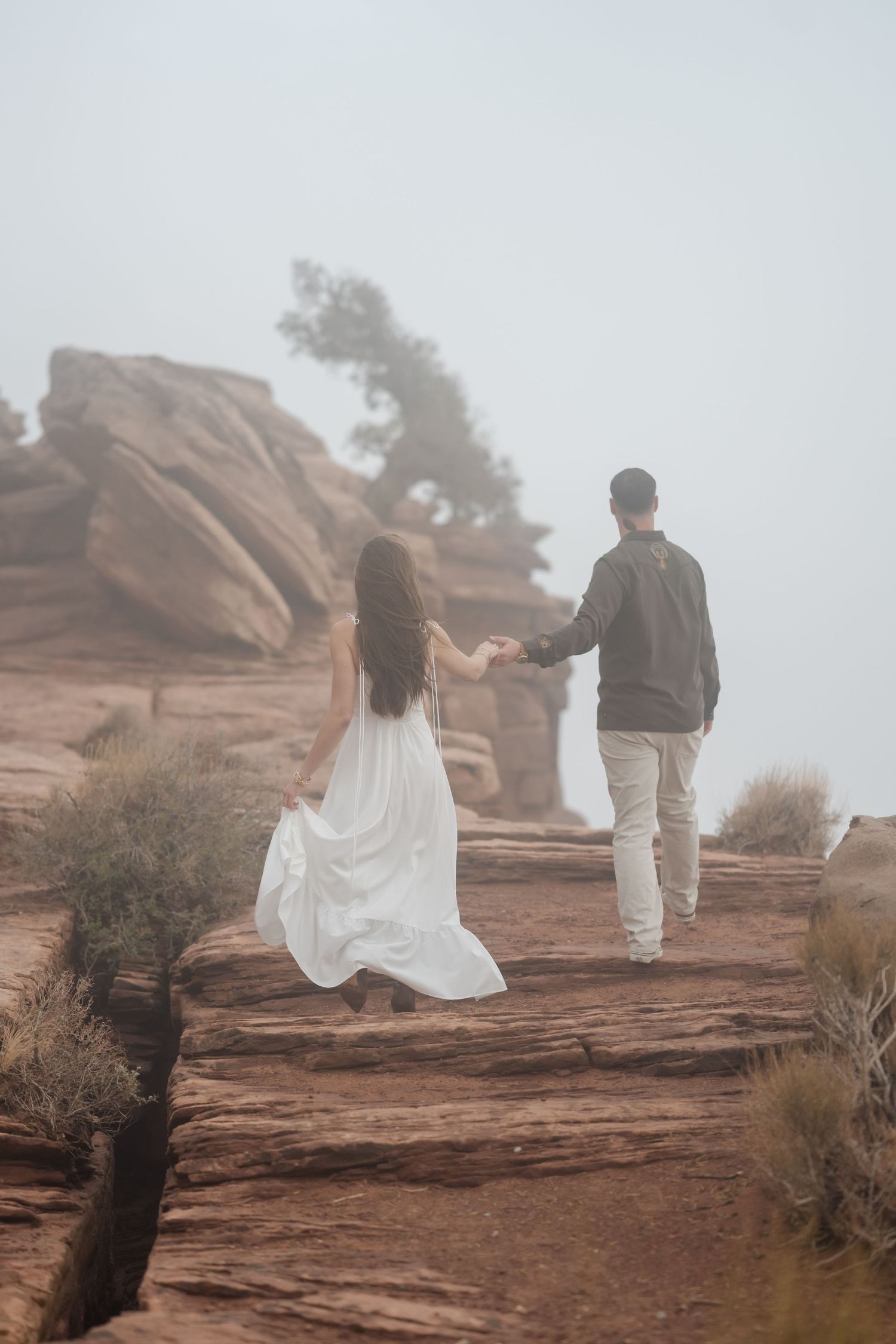 Couple walking along misty desert rock formations in formal attire.