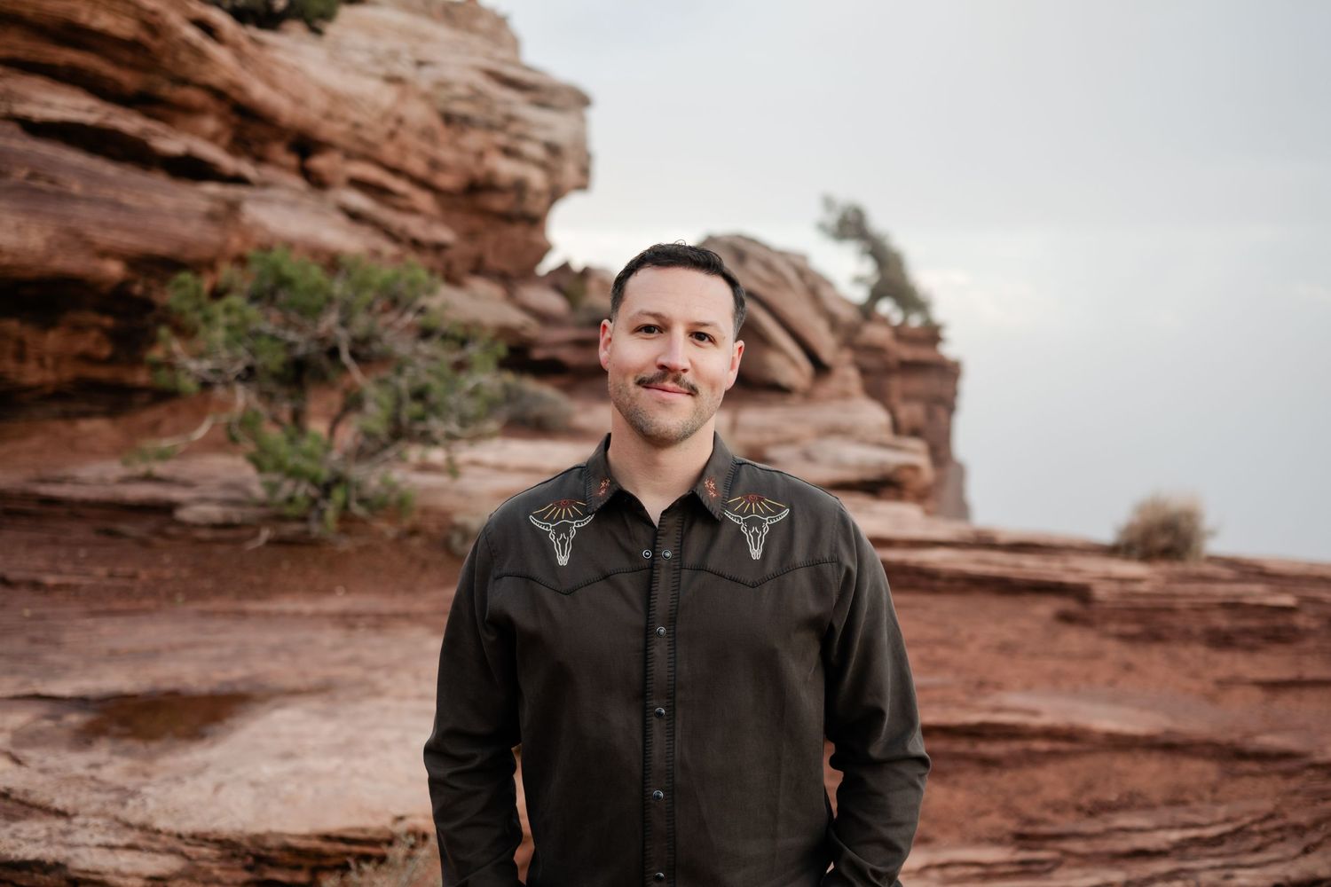 Person wearing western-style embroidered shirt standing in front of red rock formations.
