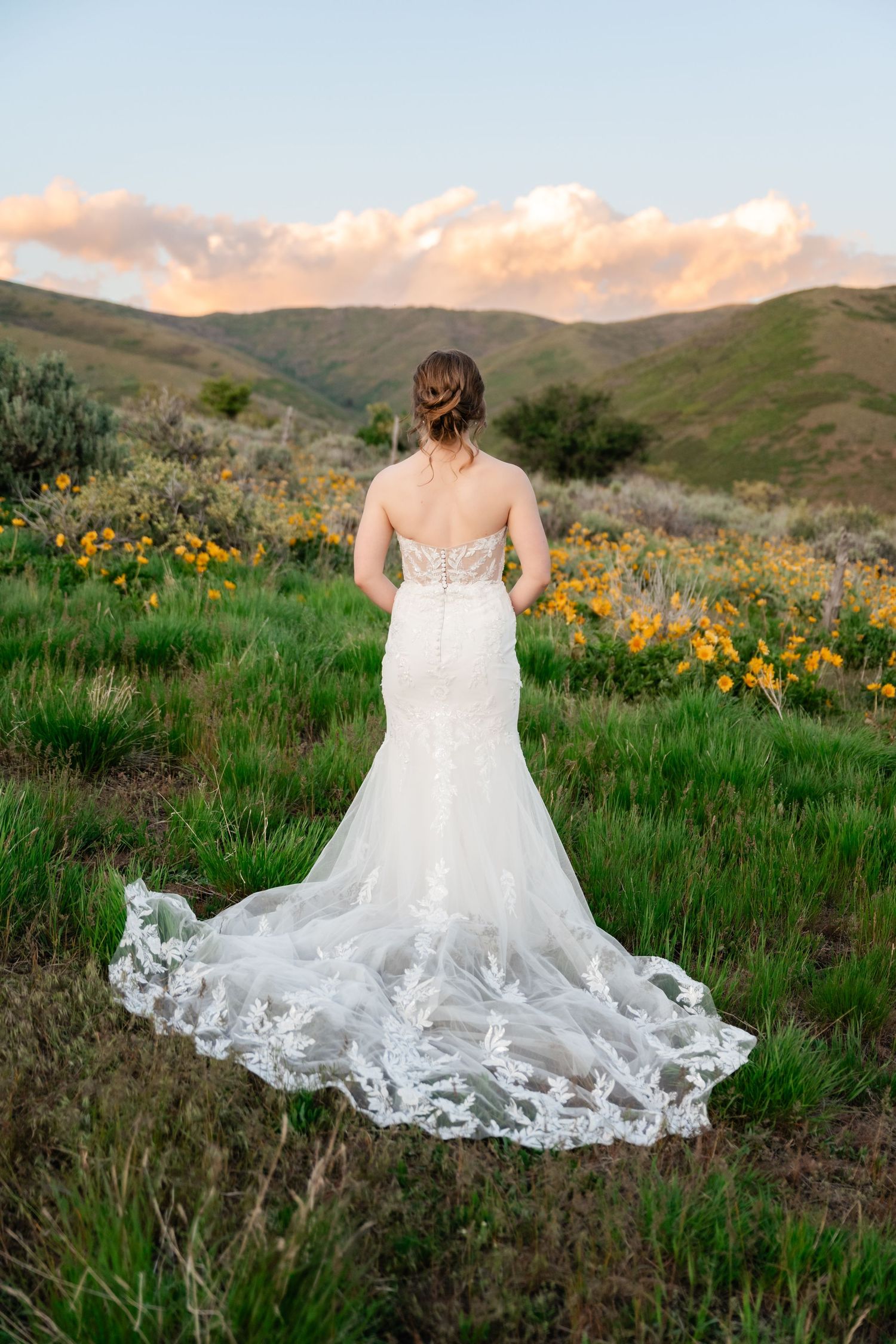 Elegant lace wedding dress train displayed against mountain wildflower landscape.