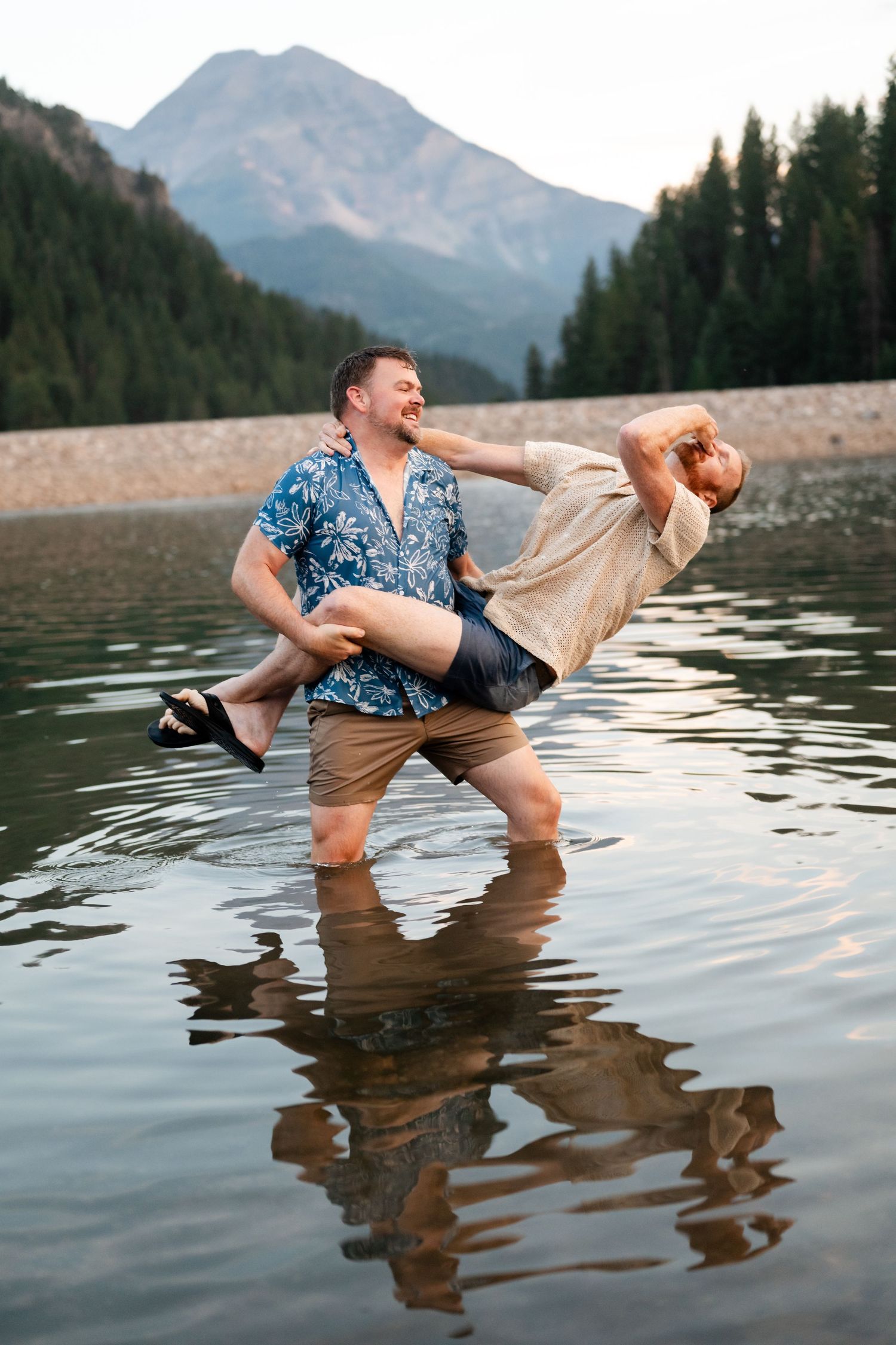 Couple having a water fight at Tibble Fork. Two men laughing and playing in a mountain lake, one carrying the other in a fun outdoor moment.