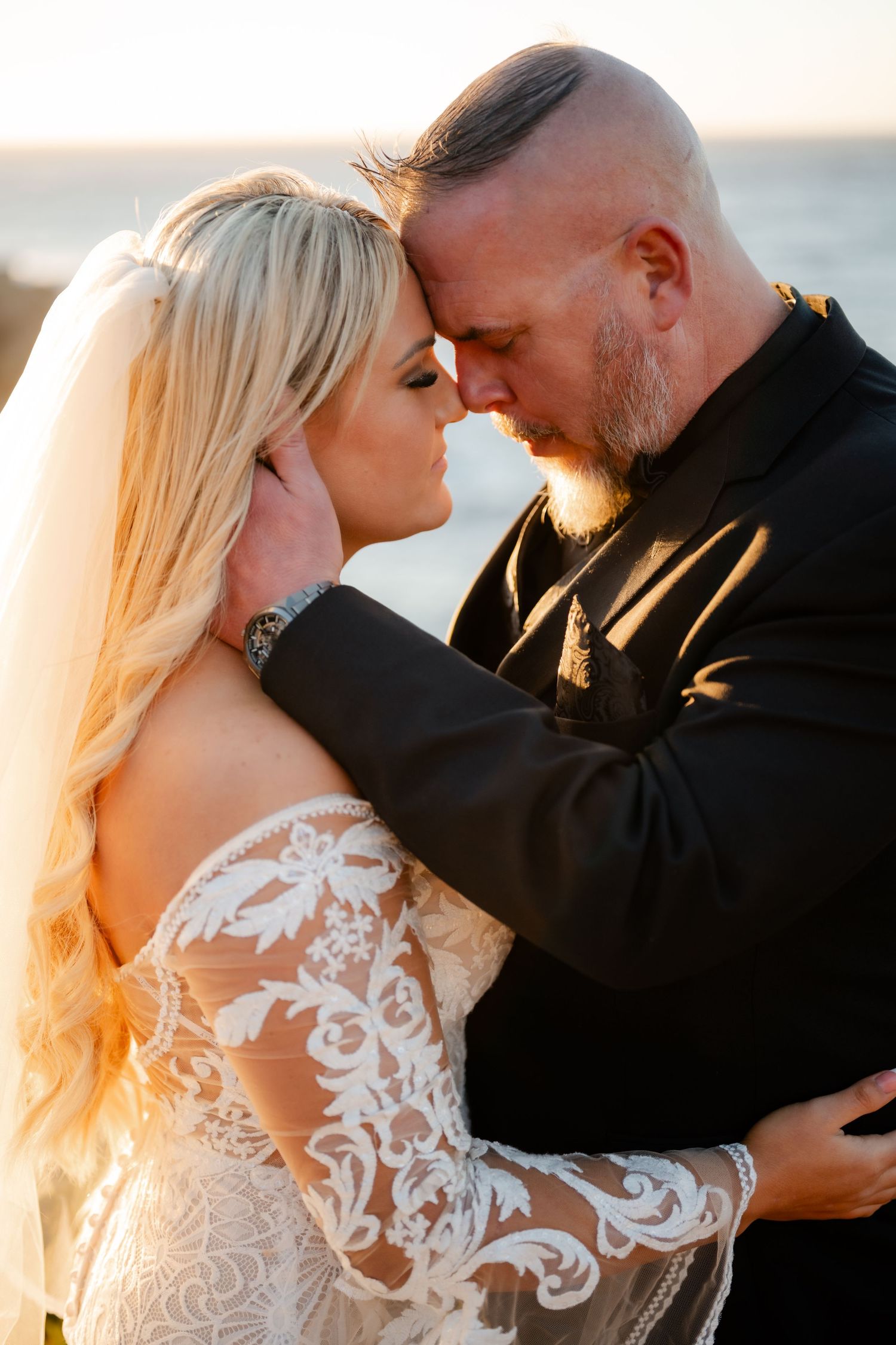 A tender wedding moment captured at golden hour against an ocean backdrop.