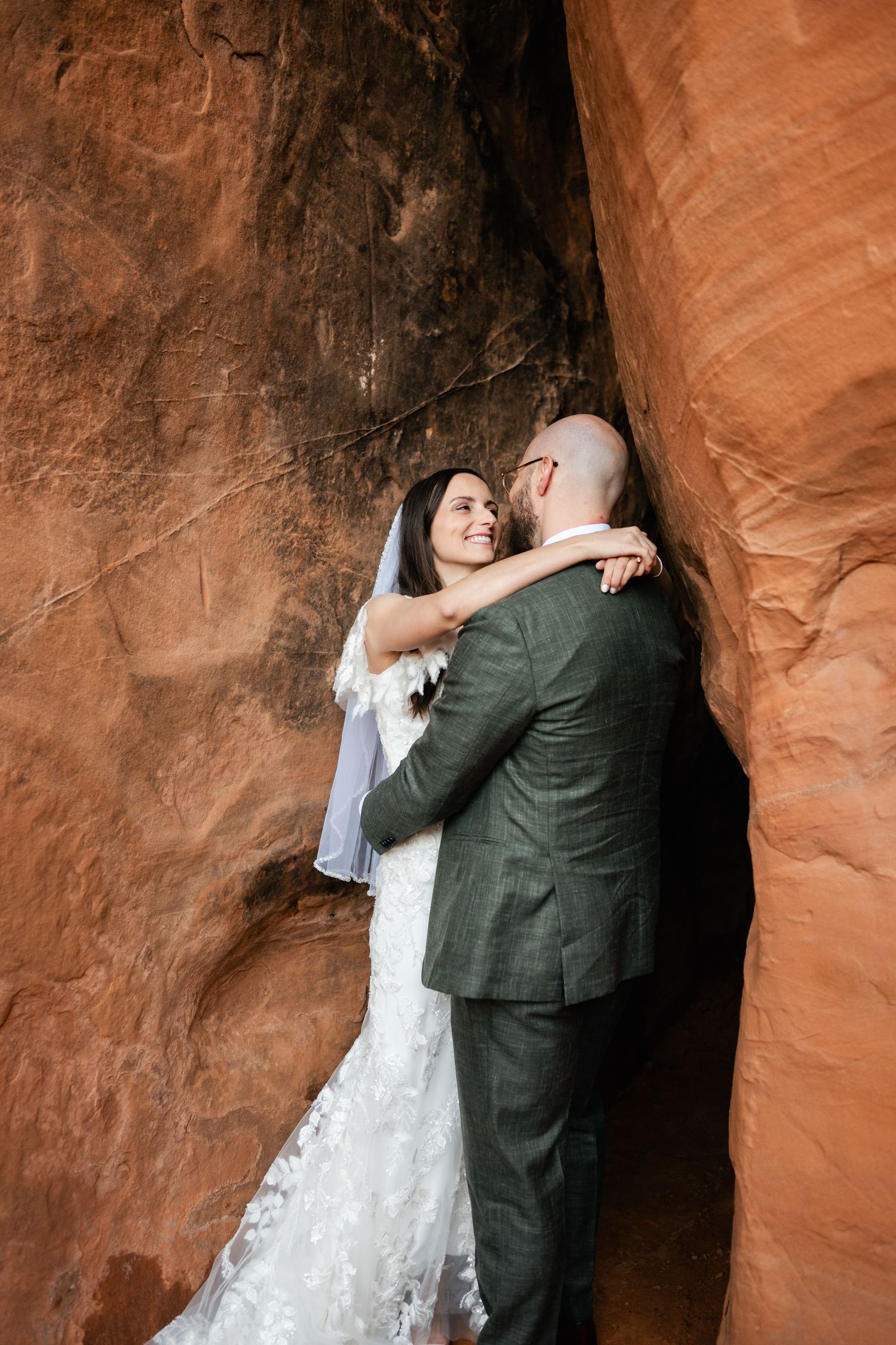 Intimate wedding couple embraces against dramatic red sandstone canyon walls.