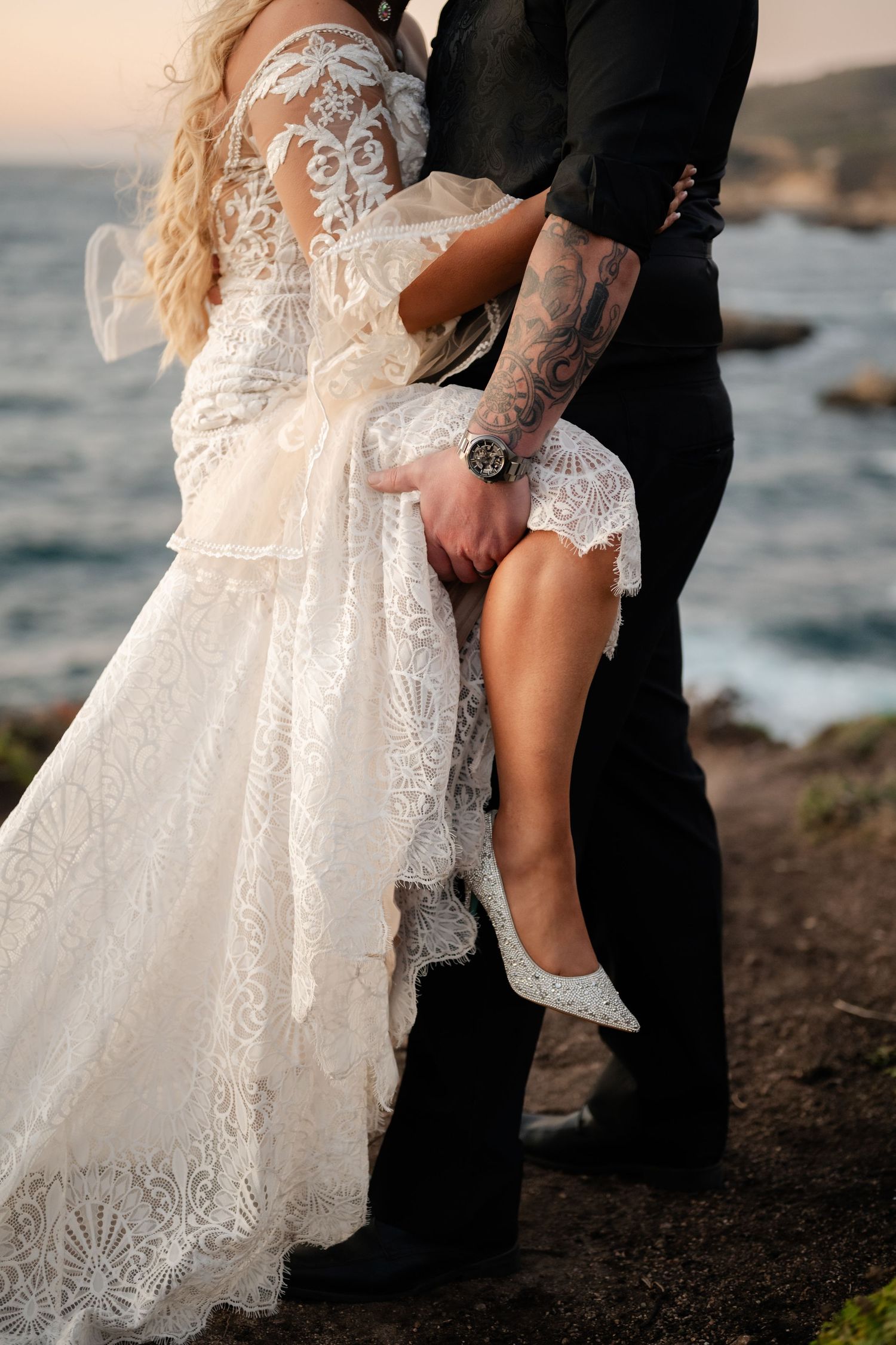 Close-up details of an intricate lace wedding dress against a coastal backdrop during sunset.