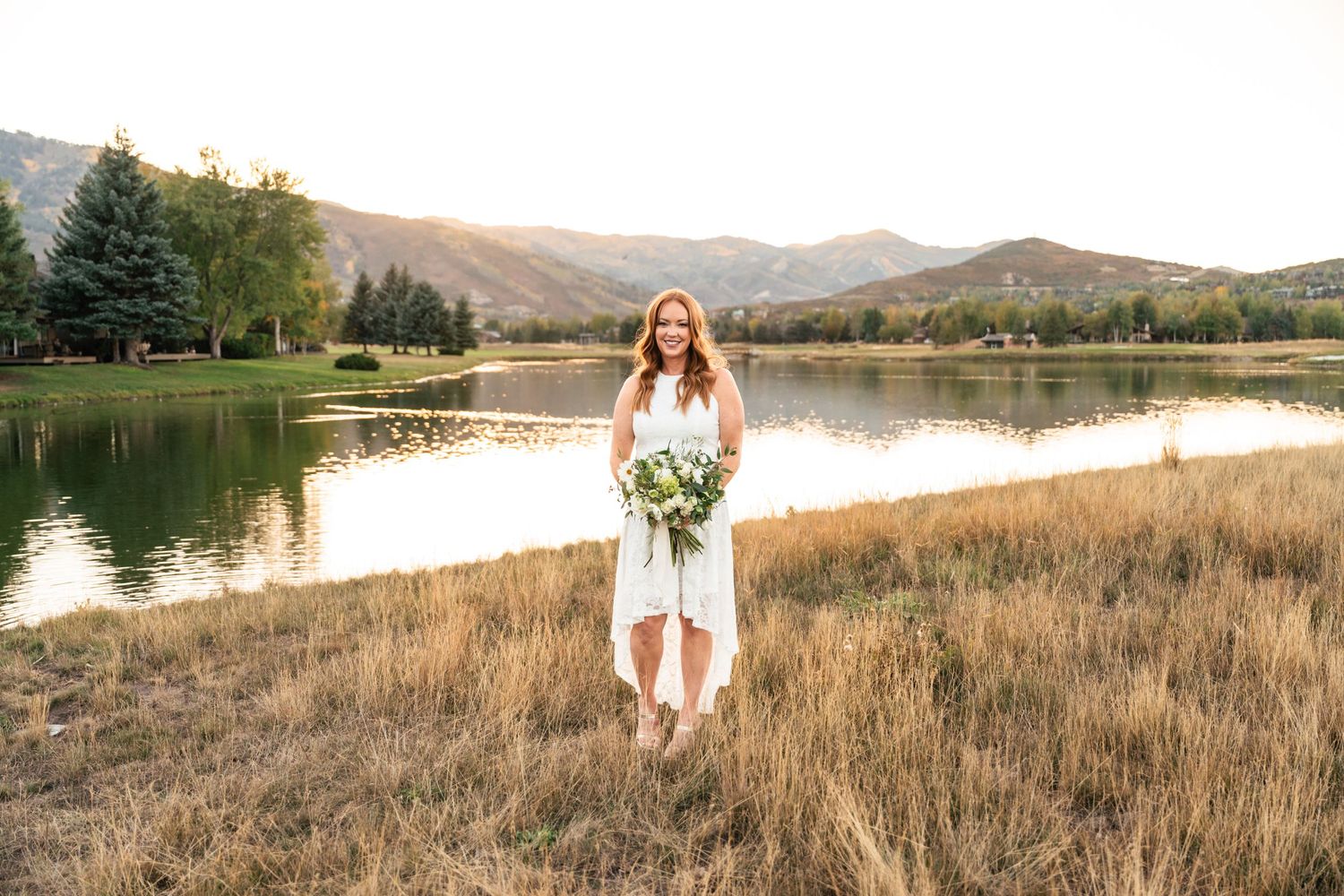 A scenic lakeside landscape with mountains and golden light in the background.