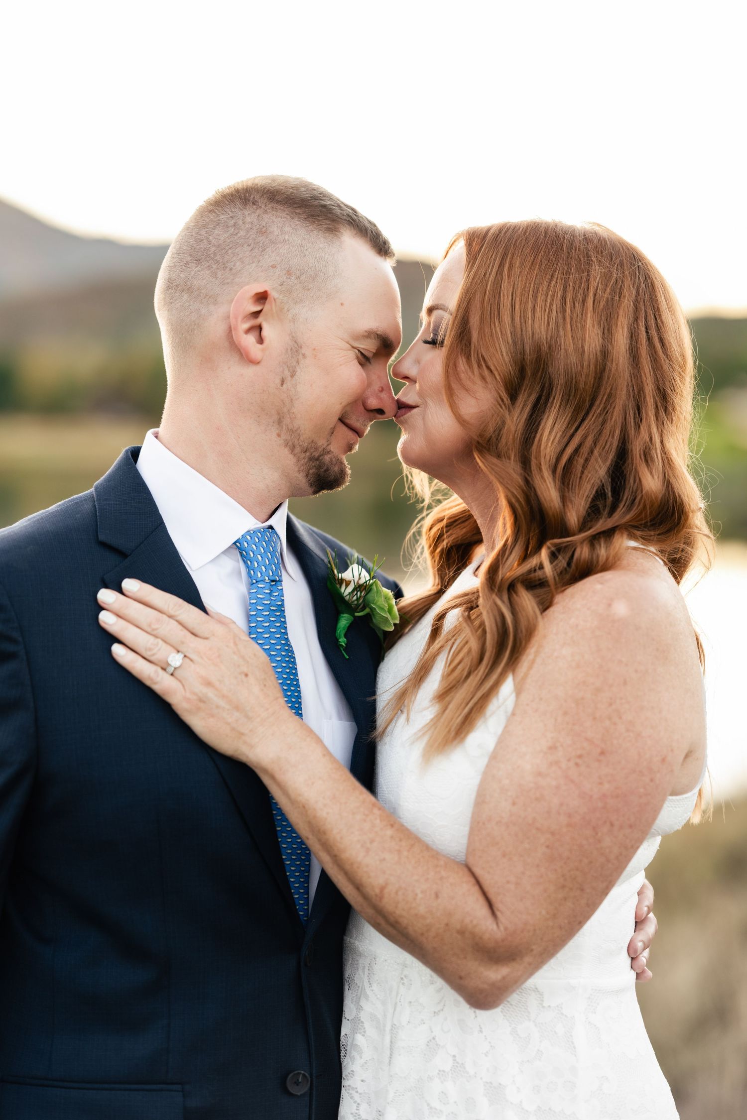 A tender moment between newlyweds against a sunset backdrop in formal wedding attire.