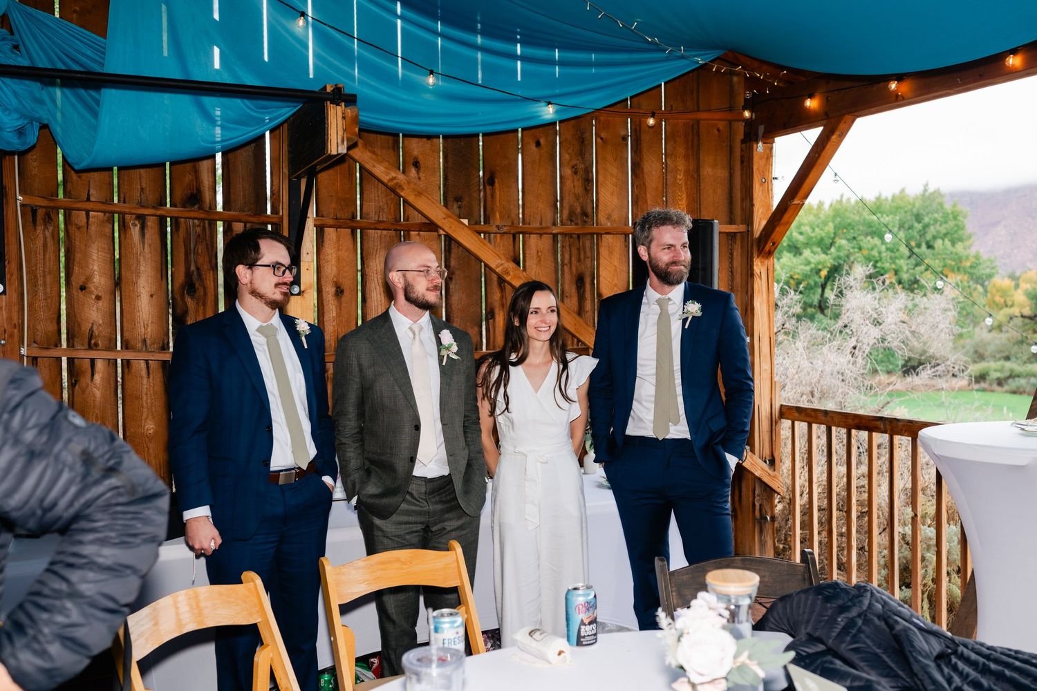 A group celebrating at an outdoor wedding reception under blue fabric draping and wooden beams.