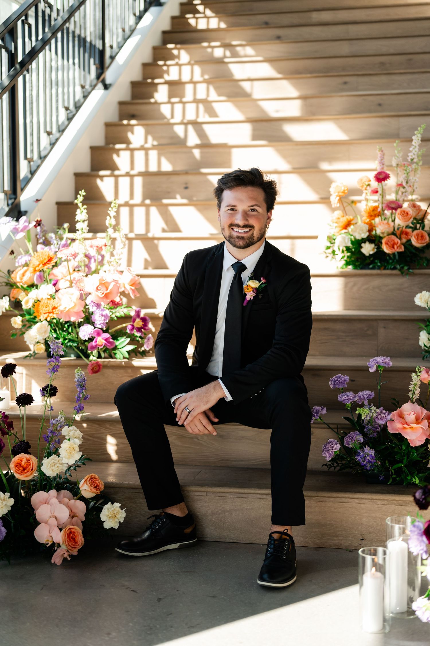 A series of black and white formal portraits with colorful floral arrangements in a sunlit wooden staircase at Enchanted Events Venue.