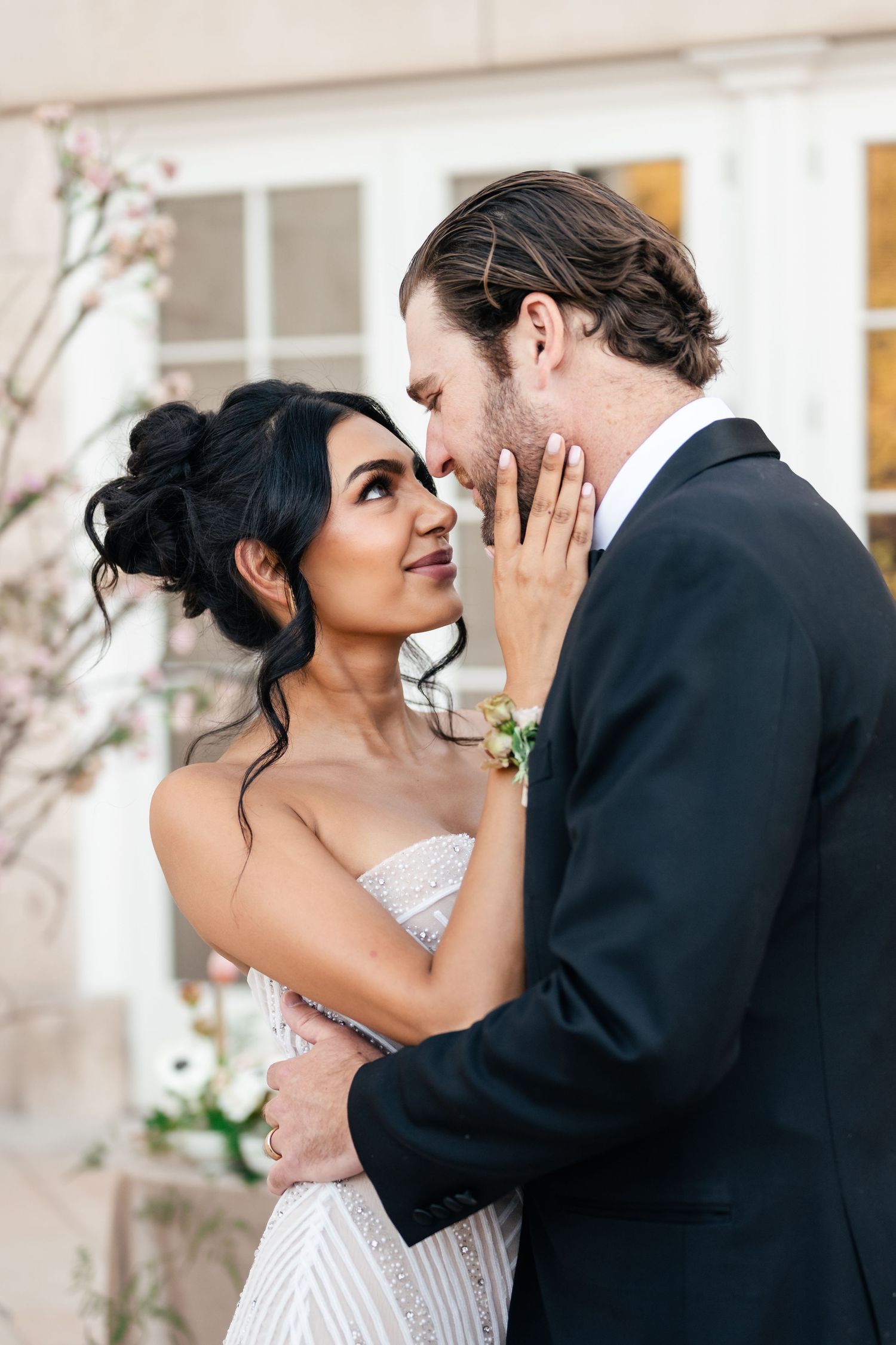 A romantic wedding couple embraces intimately while the bride in white lace gently touches her groom's face.