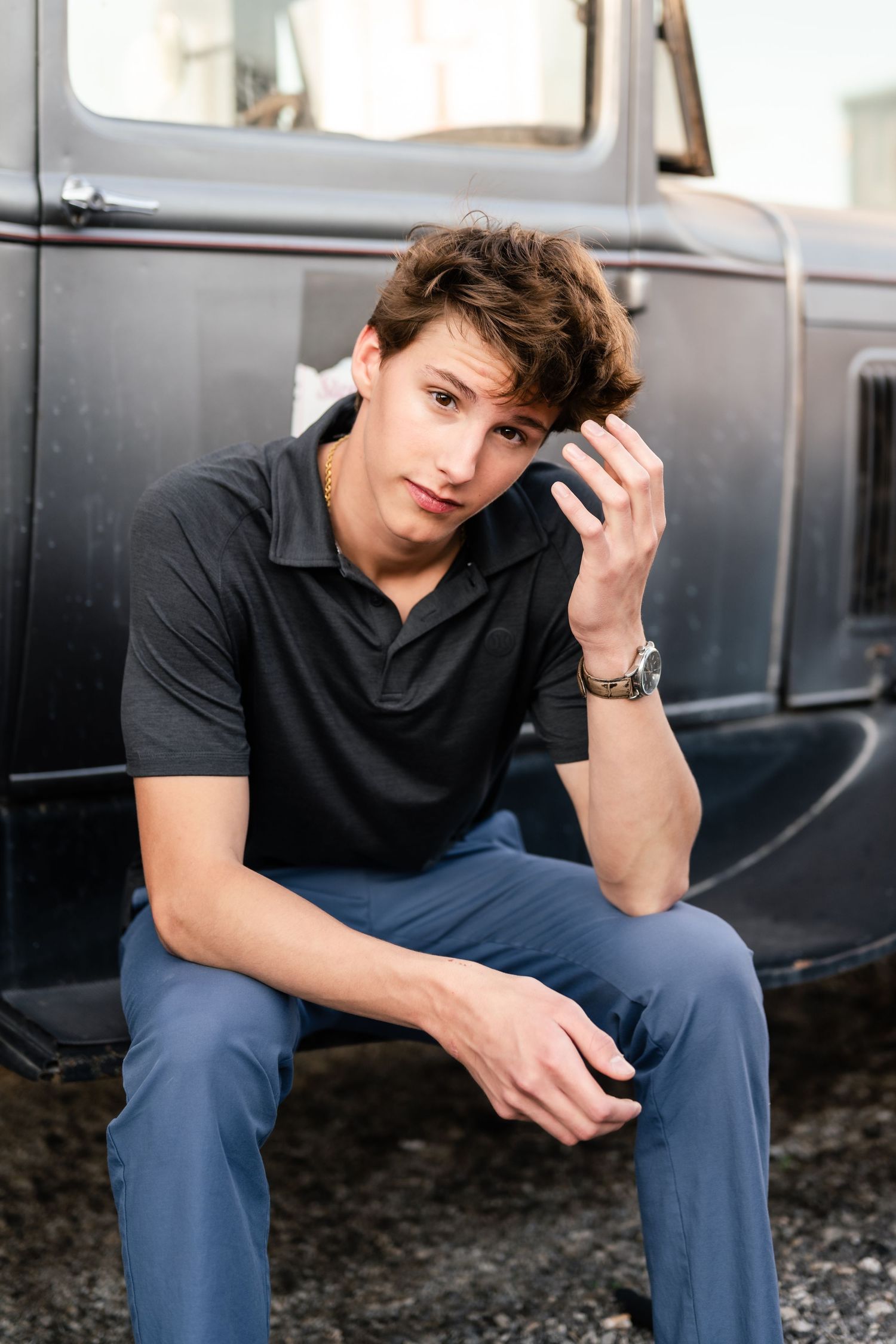 A person in a black t-shirt and blue jeans sits thoughtfully on a dark bench in an urban setting.