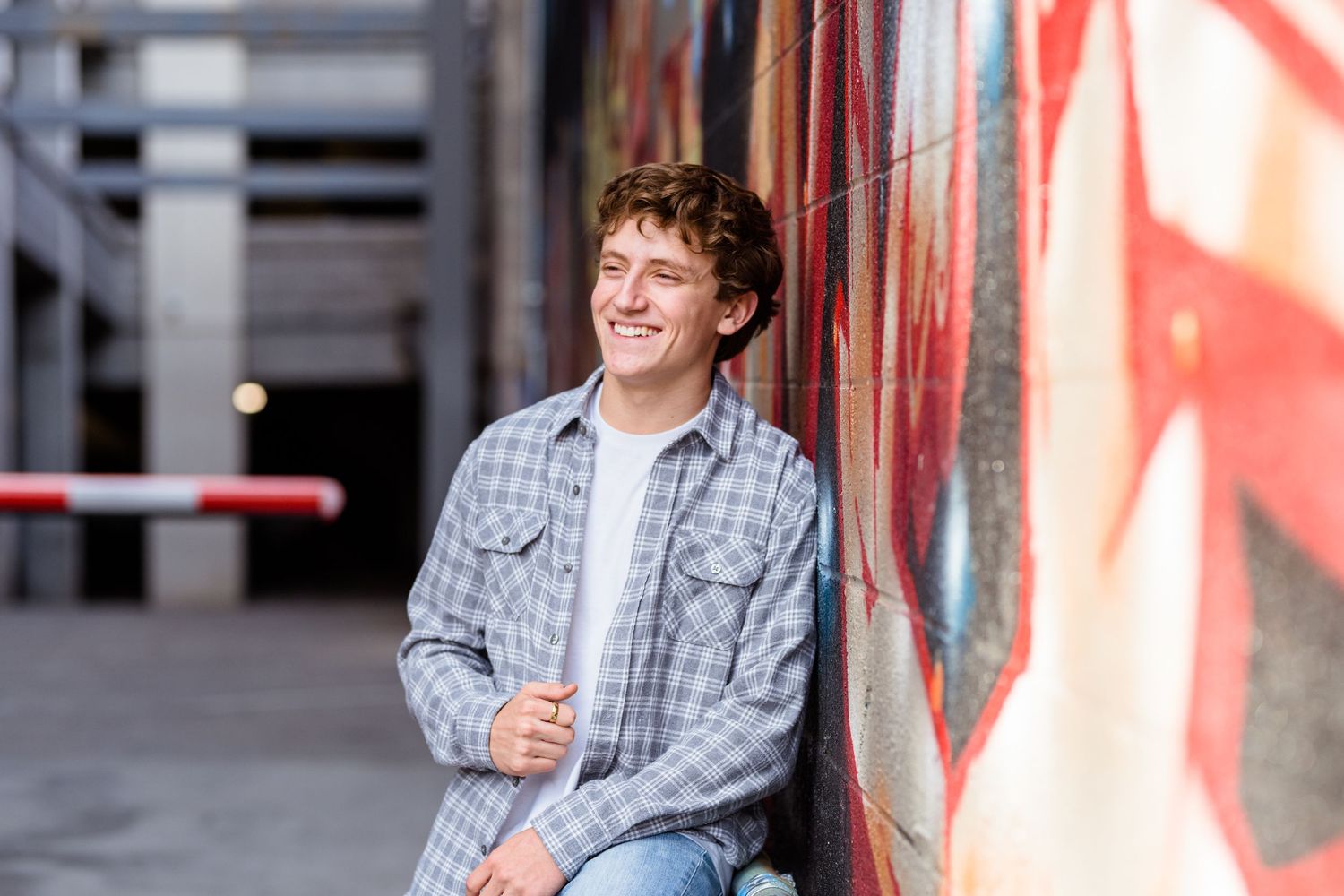 A person in a plaid shirt stands smiling against a red and gray wall background.