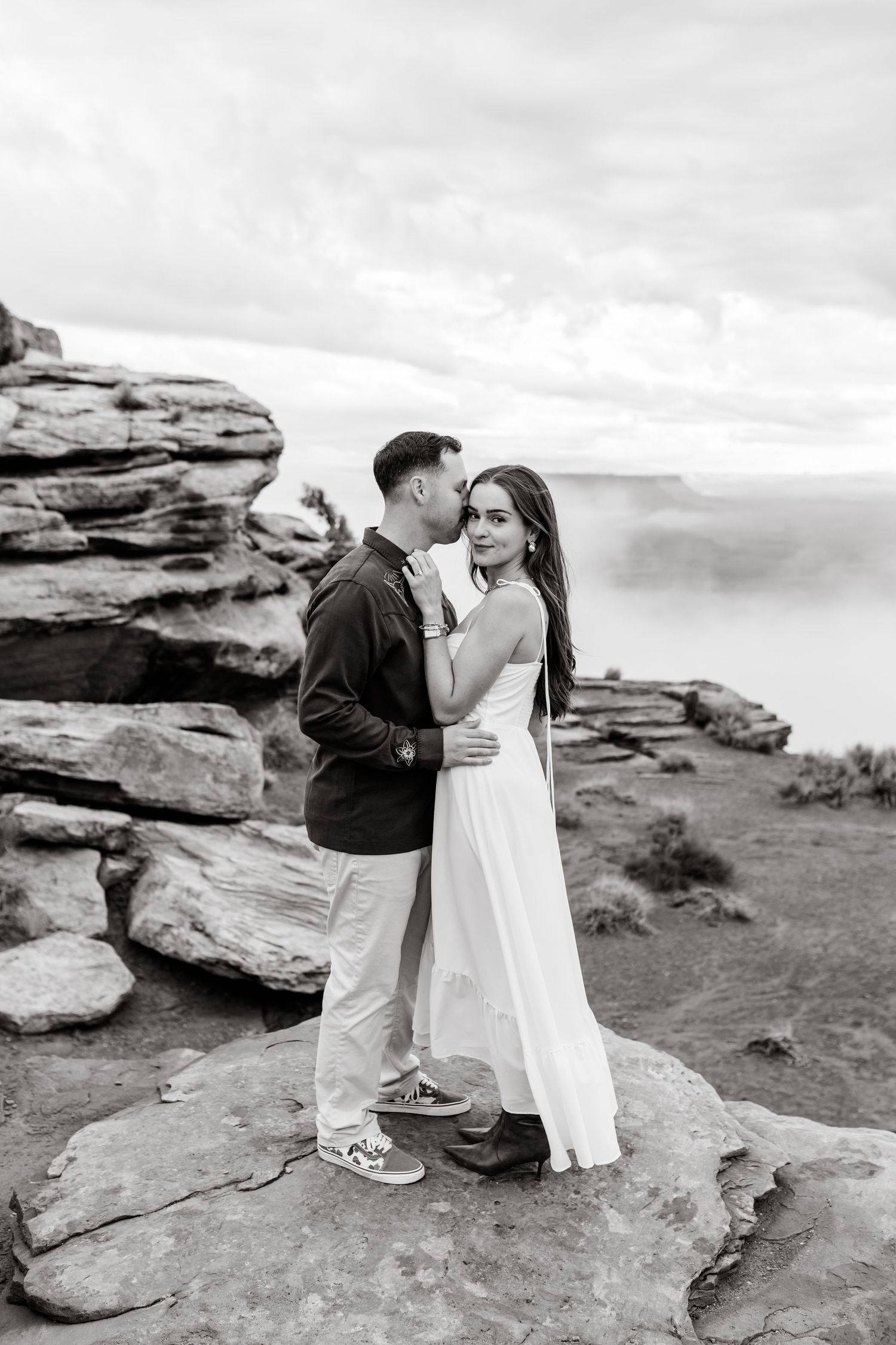 A romantic moment shared on rocky cliffs overlooking a vast desert landscape.
