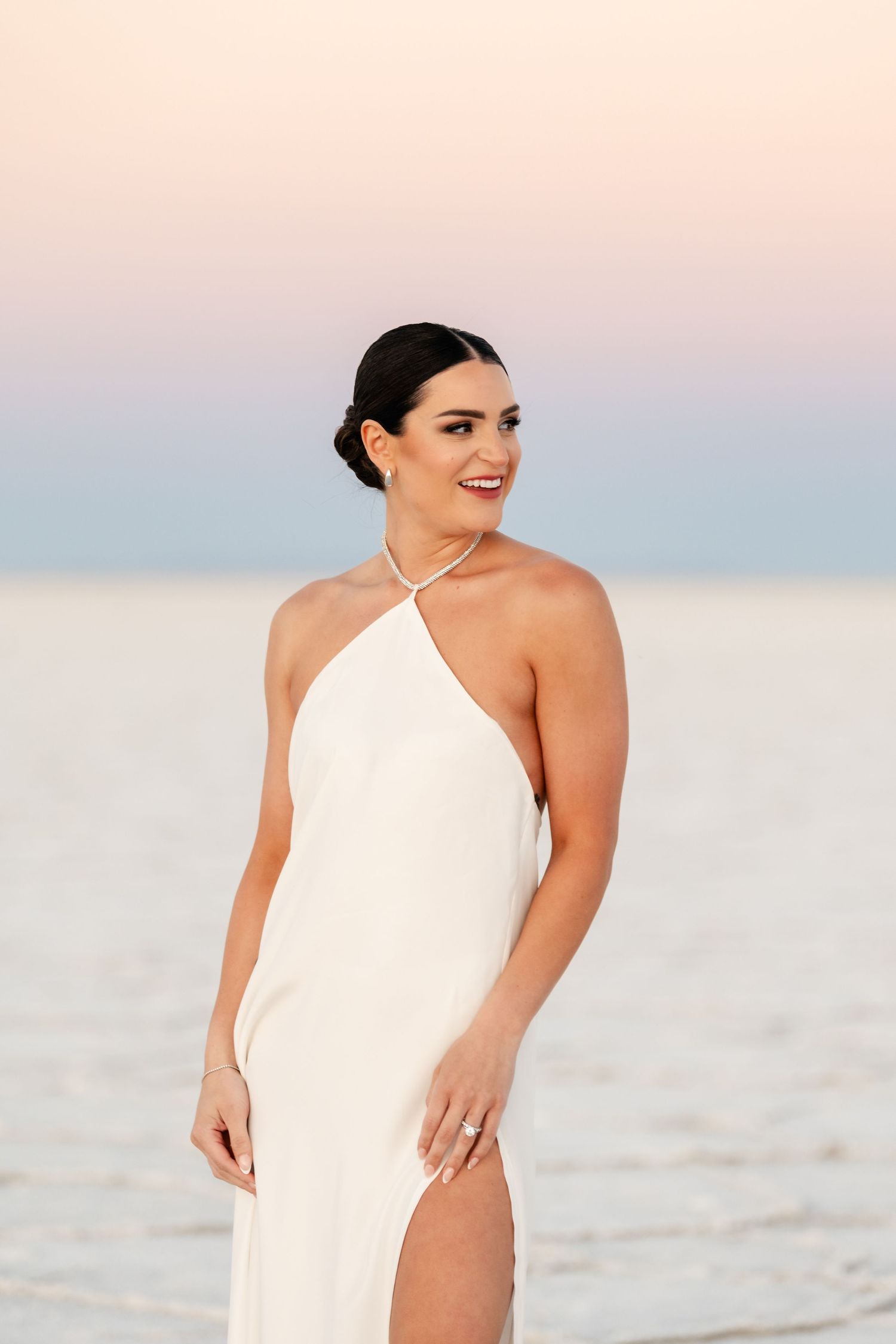 Woman in white swimsuit poses gracefully on beach at sunset with soft pastel sky in background. Utah Salt Flats Photographer.
