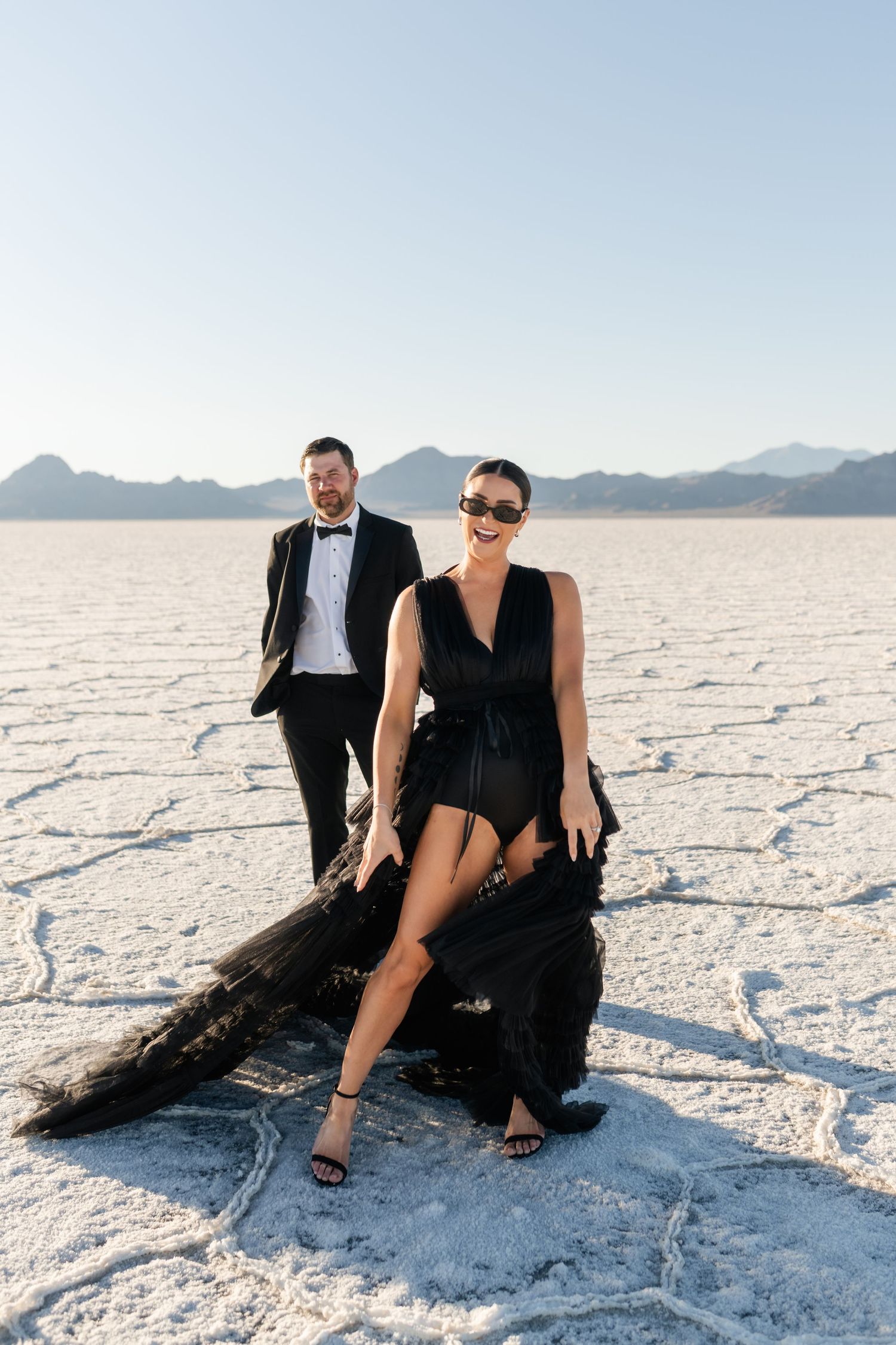 Salt Flats Photographer. Elegant couple in formal attire pose on the Bonneville Salt Flats with mountains in the background.