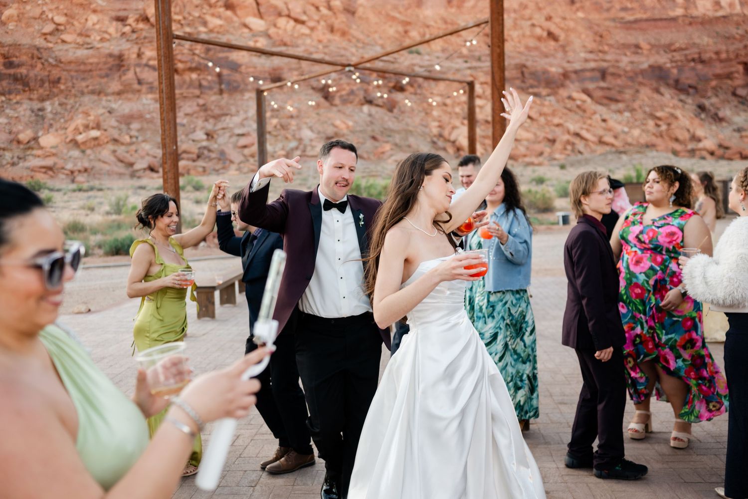 Bride and groom dancing joyfully with guests at an outdoor desert wedding reception with red rock cliffs backdrop in southern utah.