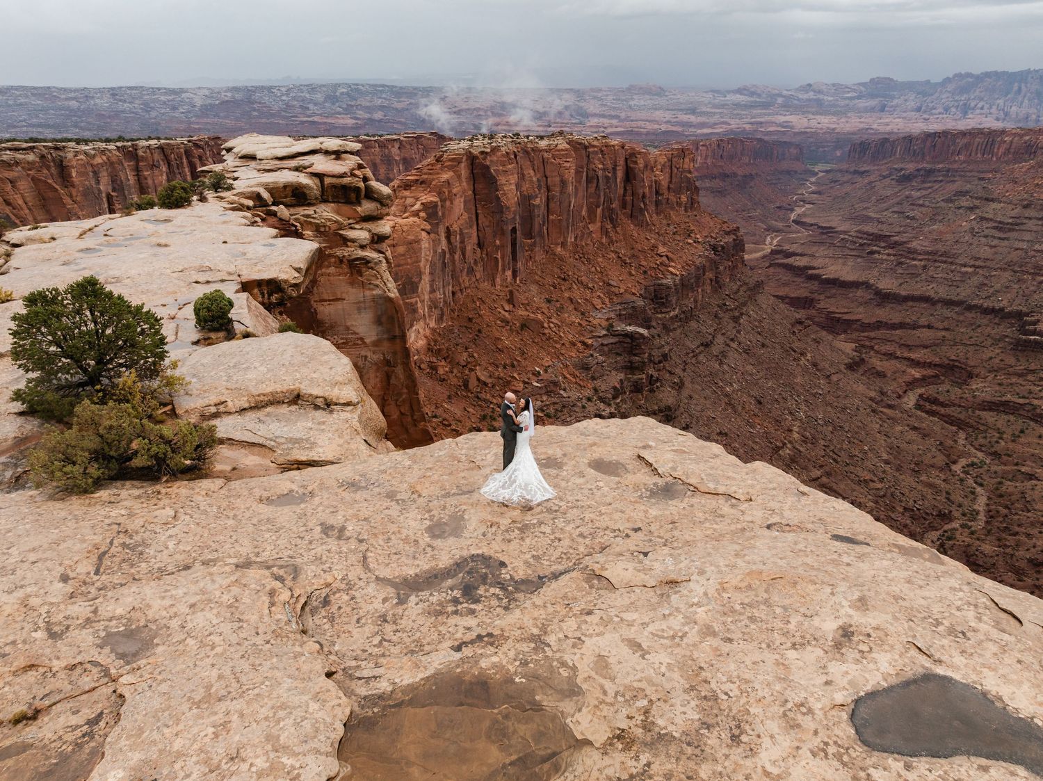 A scenic wedding photo captured at the edge of a dramatic canyon overlook in Canyonlands National Park, Utah.
