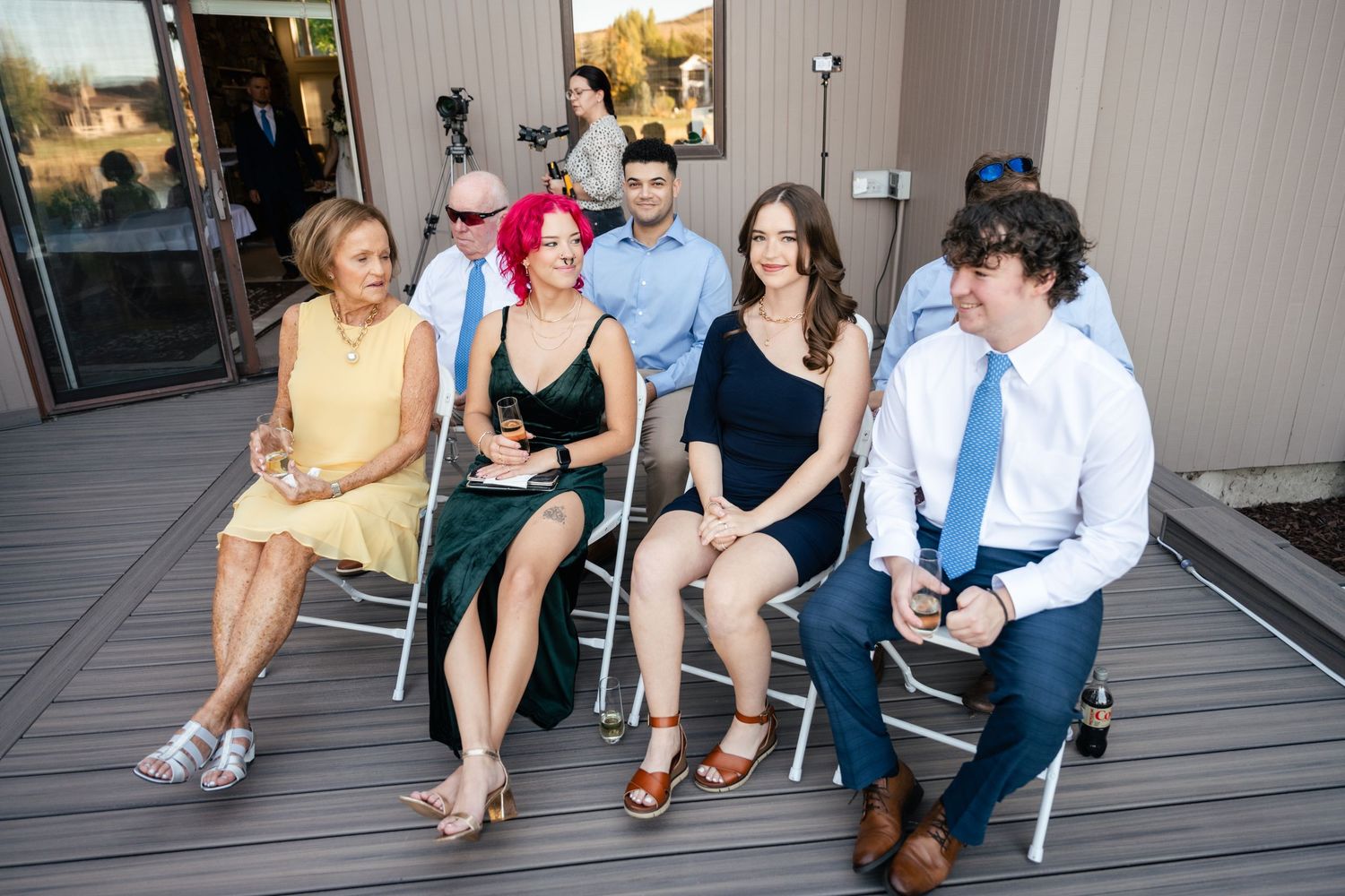 Group of wedding guests sitting and chatting on a gray deck during an outdoor celebration.