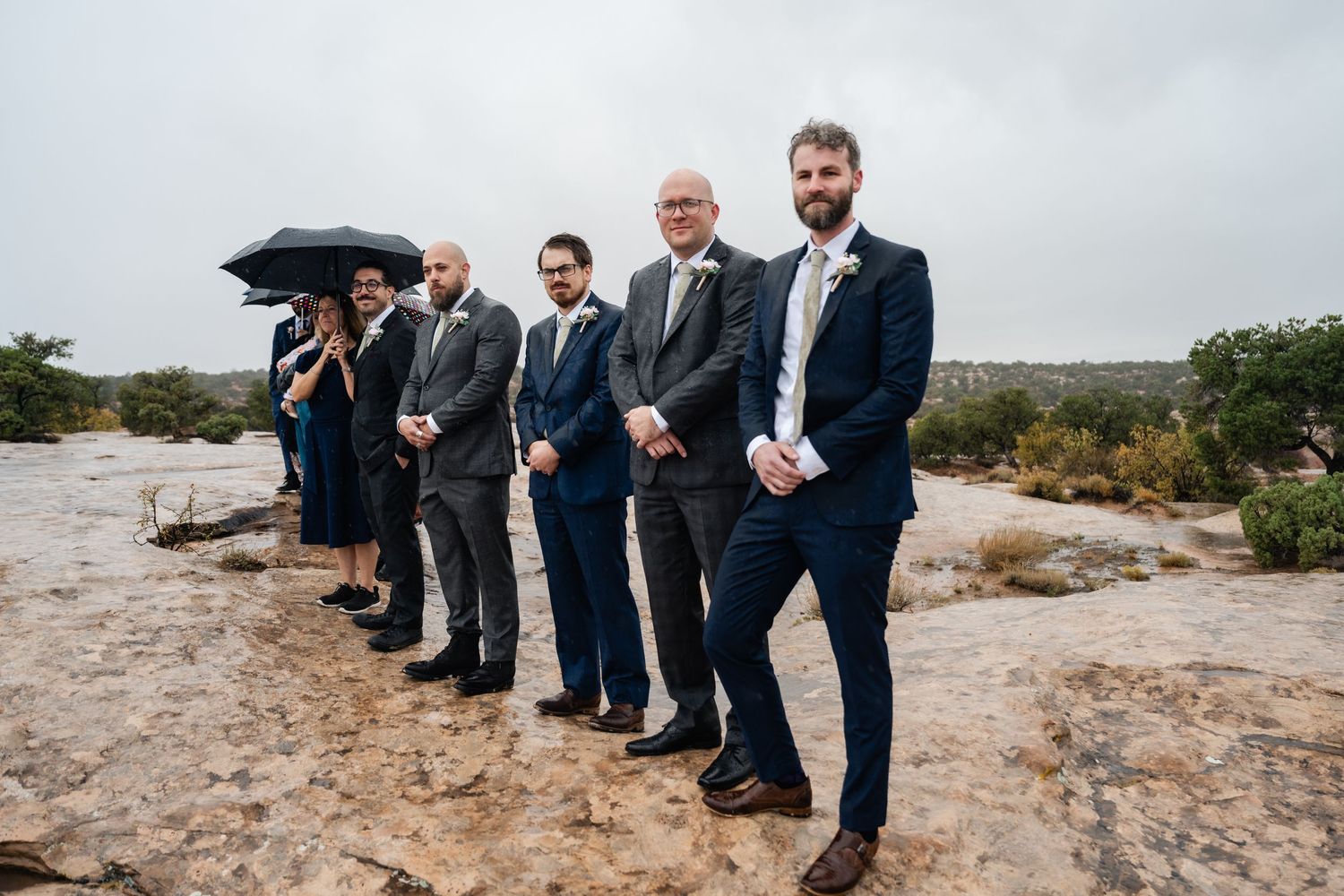 Wedding party members line up on desert cliff for formal photo.