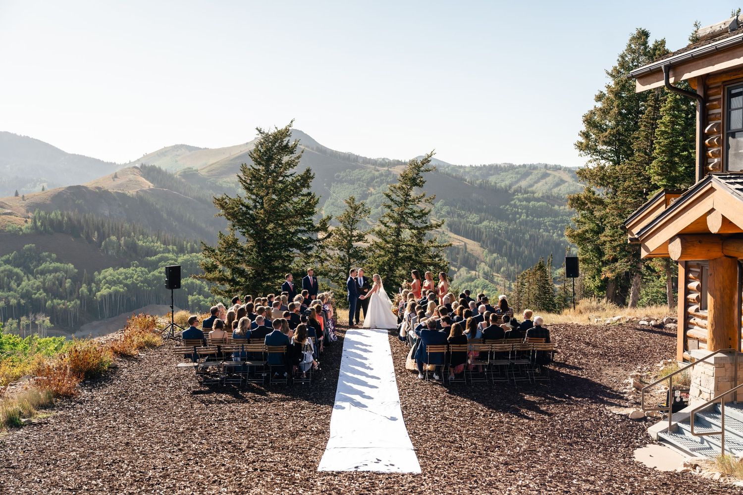 Outdoor mountain wedding ceremony with guests seated on either side of a white aisle runner overlooking scenic hillsides. Park City Wedding