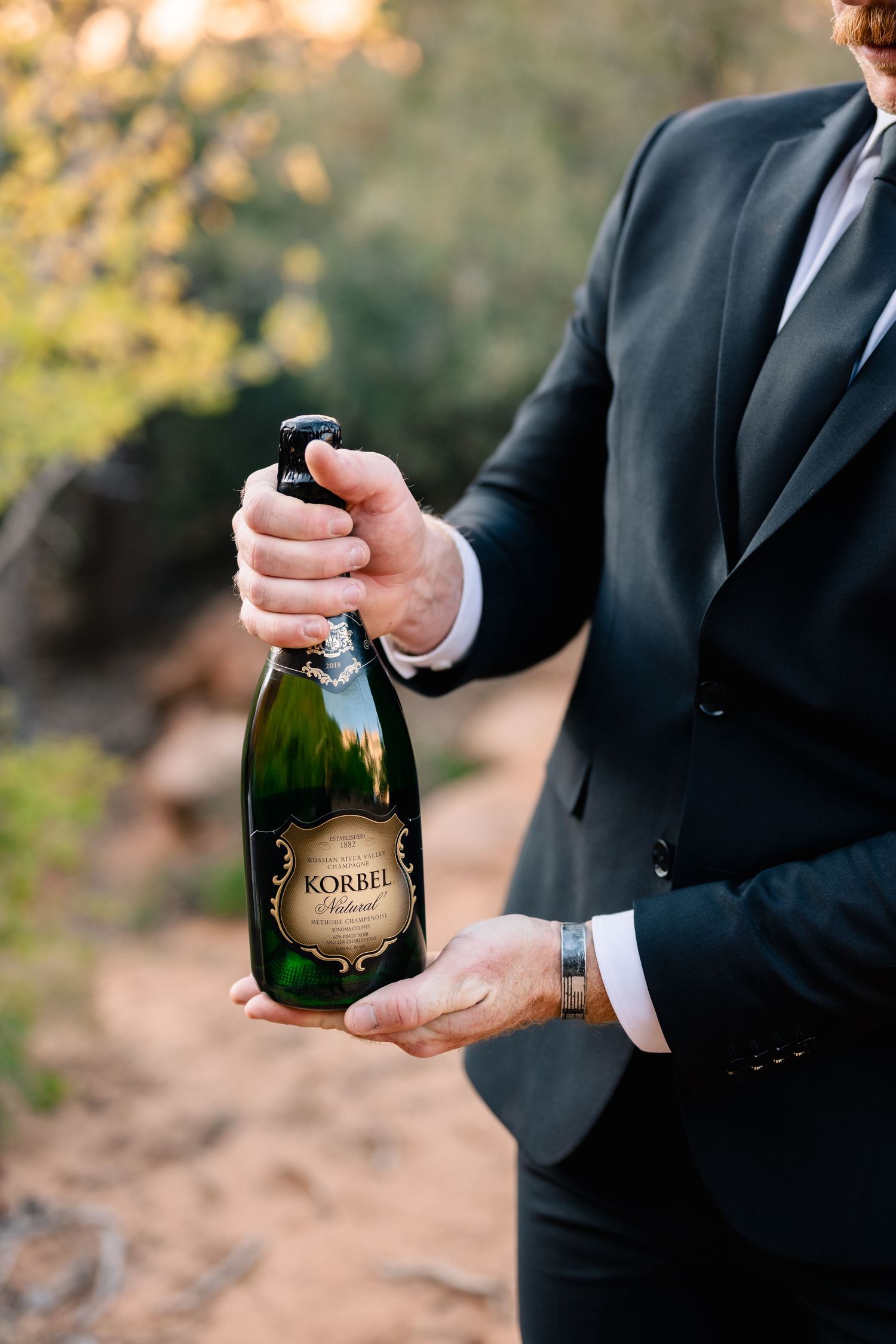 Hands hold a bottle of Korbel champagne during an outdoor celebration.