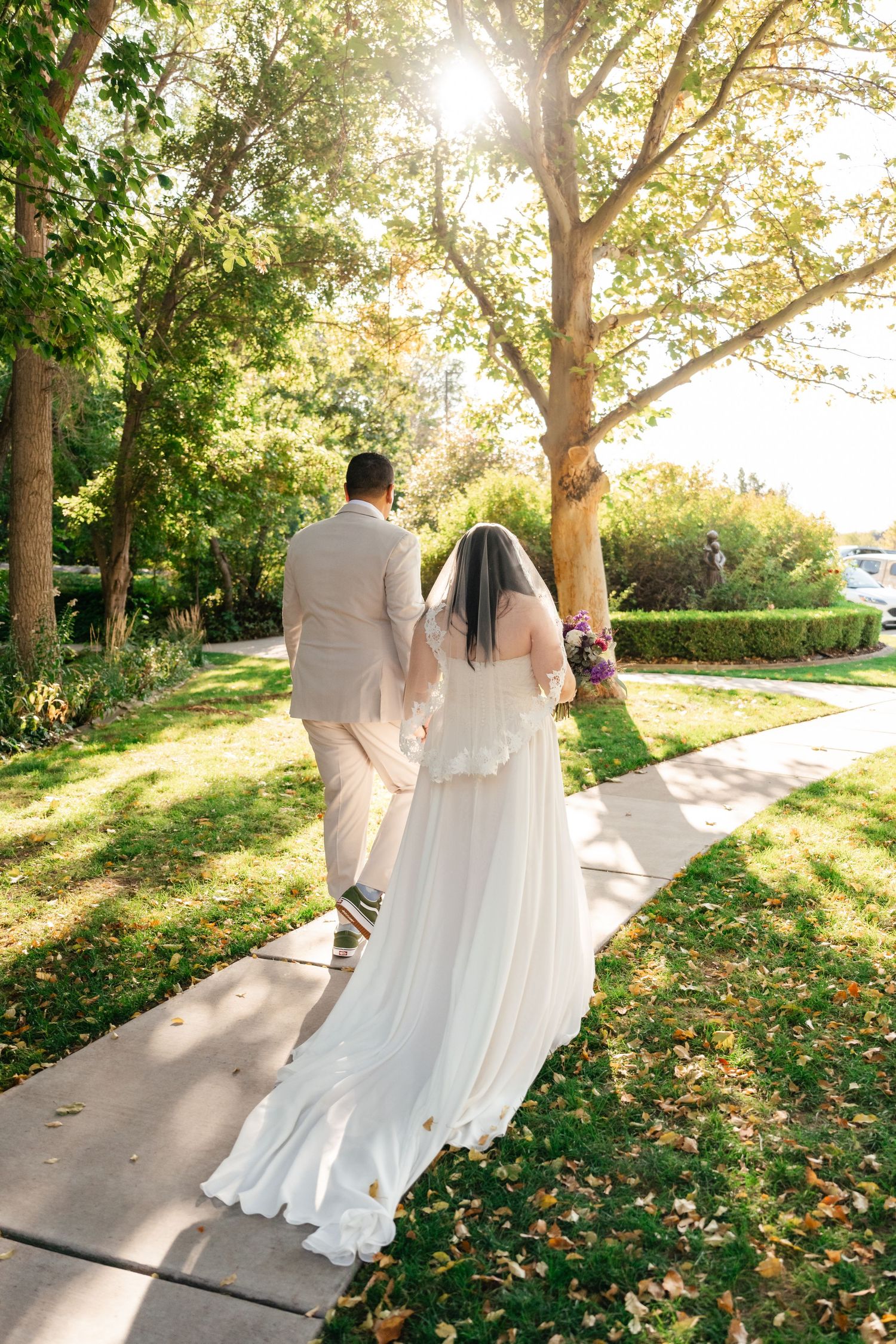 A couple walks along a sunlit garden path after their outdoor wedding ceremony.