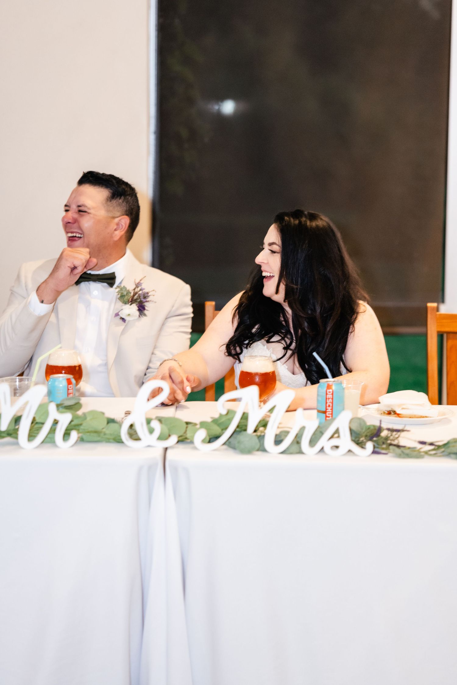 A couple shares a lighthearted moment while seated at their wedding reception head table.
