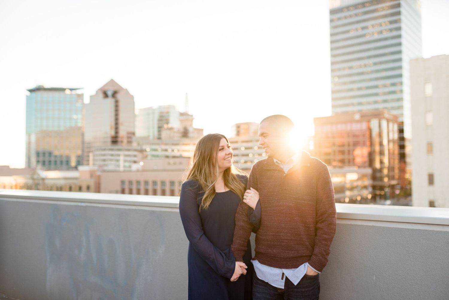 A couple sharing a tender moment on a rooftop with city skyline at golden hour.