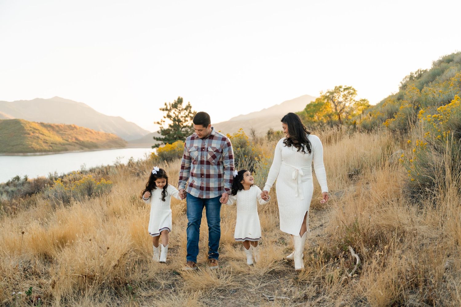 A couple and their dog walk along a scenic hillside trail at golden hour while taking engagement photos.