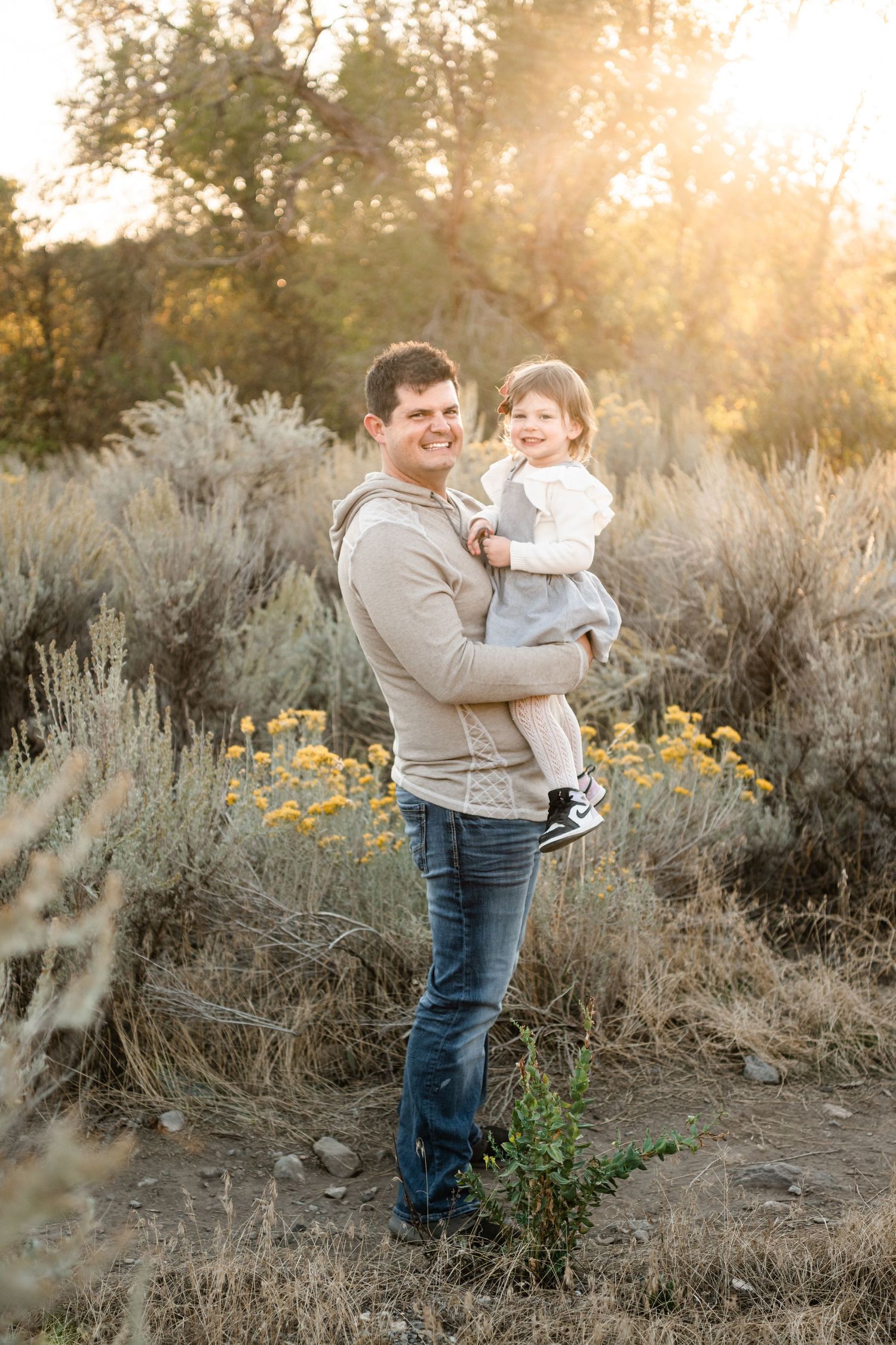 A heartwarming outdoor family photoshoot in a field of sagebrush and wildflowers during golden hour sunset.